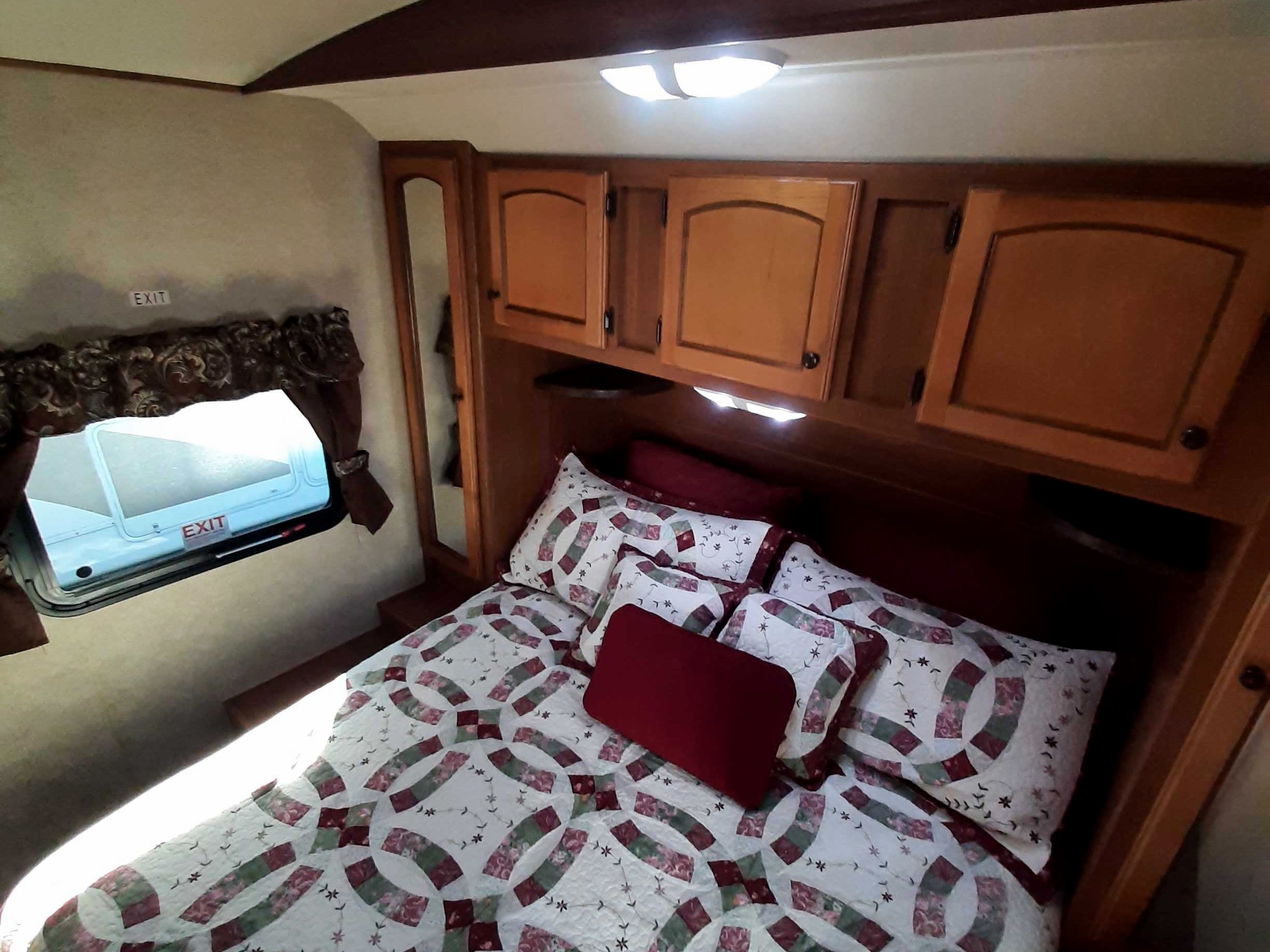 Cozy RV rental interior: bedroom with patterned bed, overhead cabinets & visible exit signs.. Crossroads RV Sunset Trail 2013