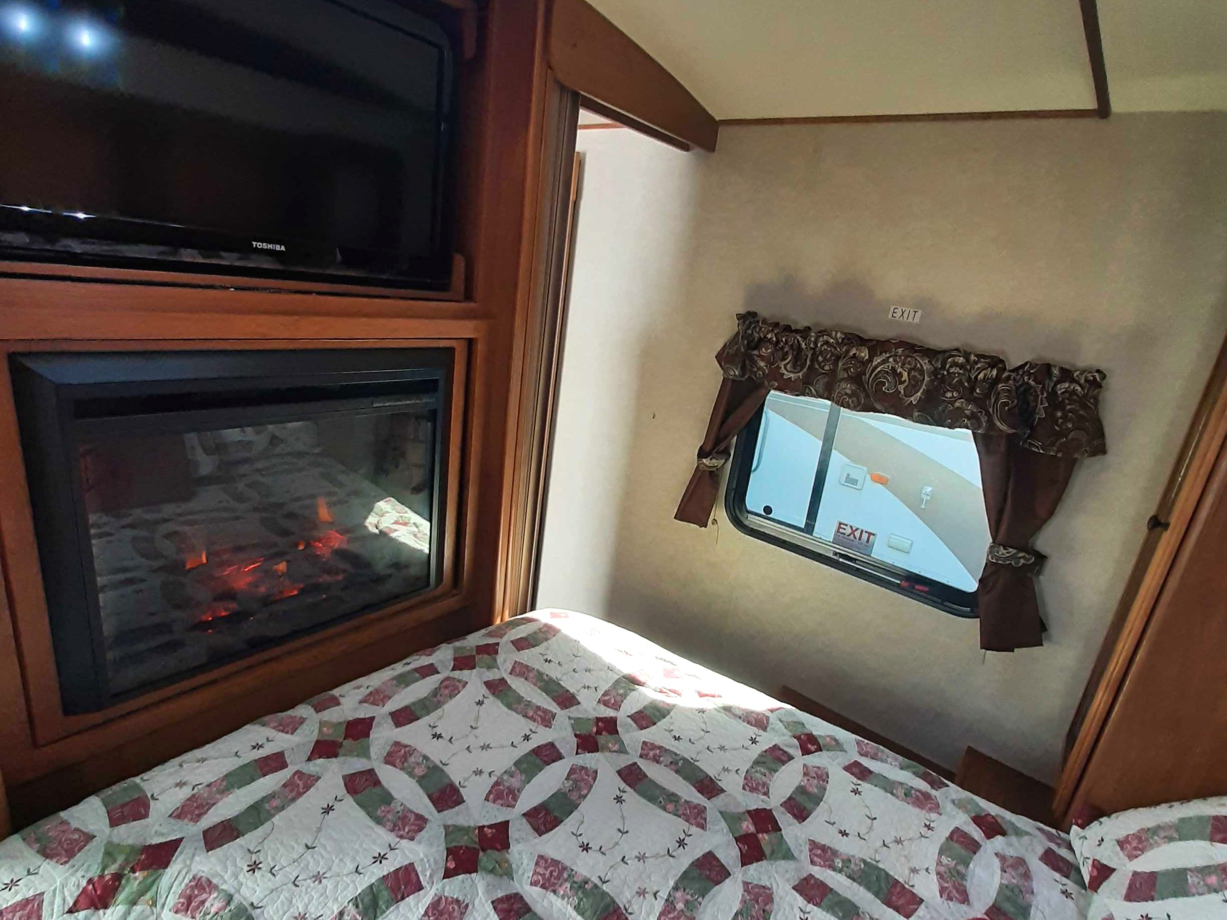 Enjoy the comforts of home in this cozy rv rental bedroom, featuring a TV, electric fireplace, and a quilted bedspread.. Crossroads RV Sunset Trail 2013