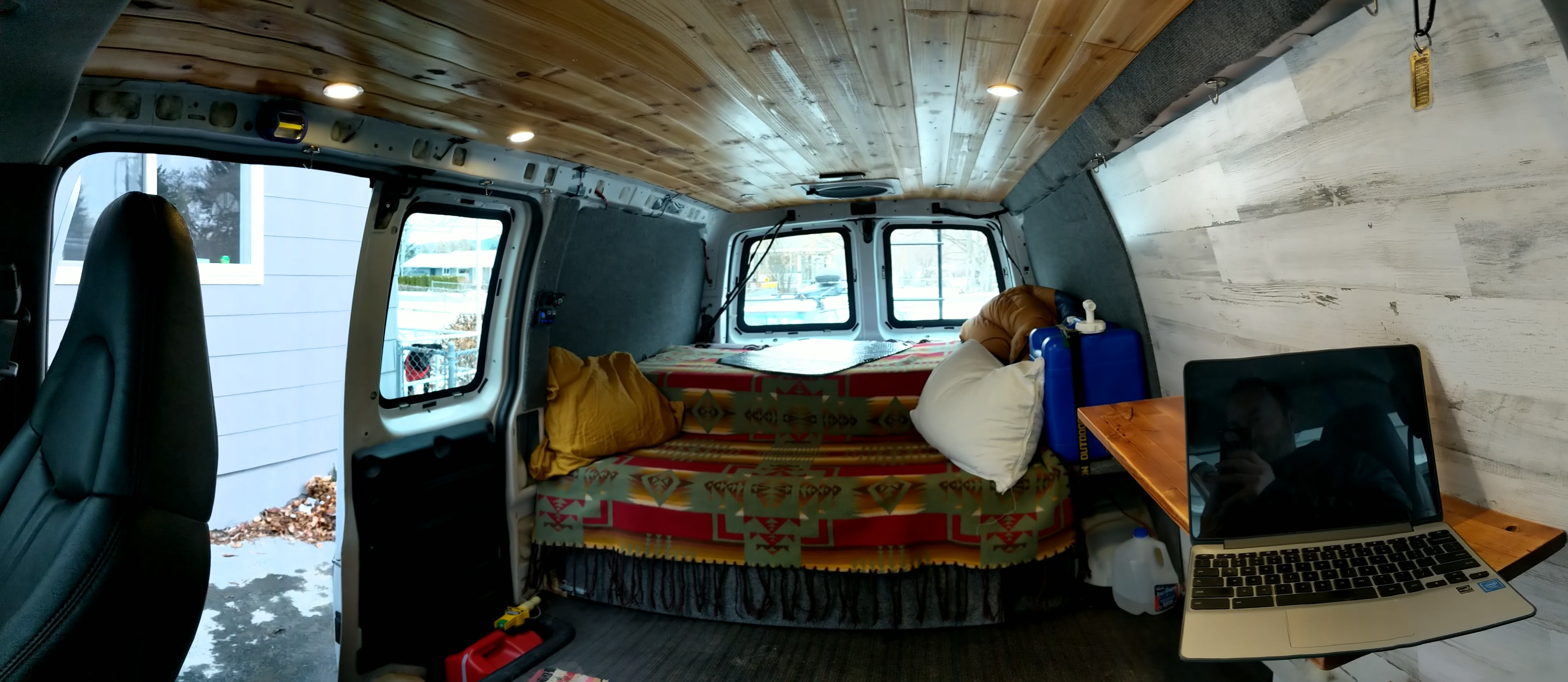 Cozy van life interior: an RV rental conversion with wood ceiling, bed, and laptop desk.. Gmc Savanna 2007