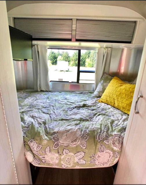 Cozy RV rental bedroom with a floral bedspread, TV, and large window. Perfect for travel adventures.. Airstream Sport 2018