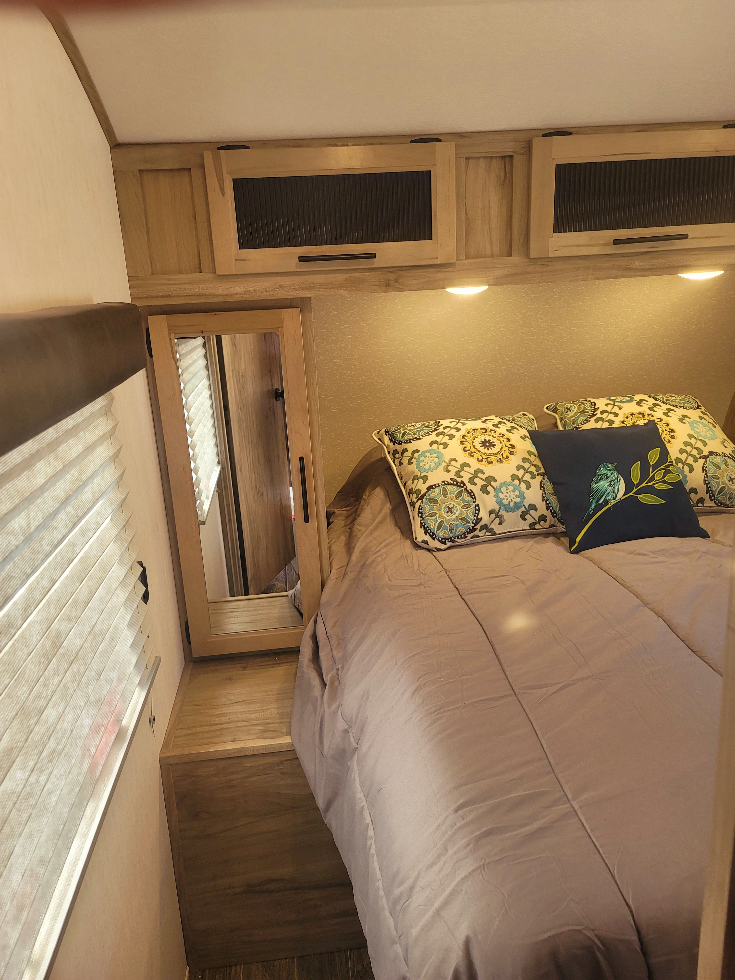 Inside an RV rental bedroom: bed with floral pillows, wood cabinetry, built-in mirror, and pleated window blinds.. Forest River Cherokee Alpha Wolf 2021