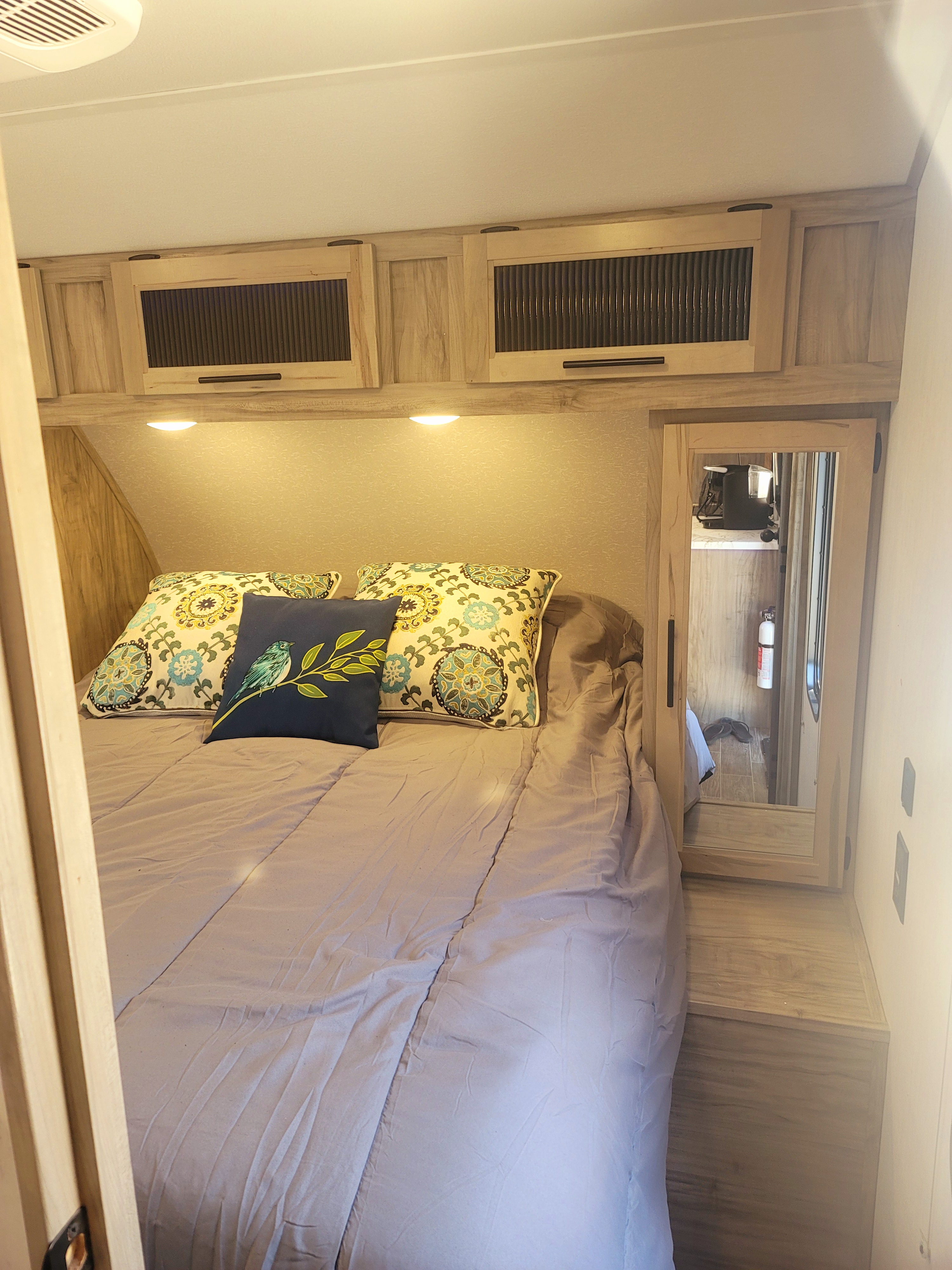 Cozy RV rental bedroom with wood cabinets, under-cabinet lighting, and mirror, featuring floral & bird pillows.. Forest River Cherokee Alpha Wolf 2021