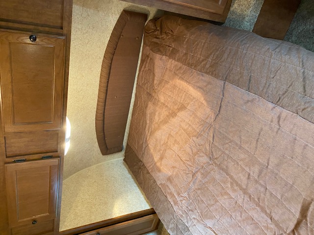 RV rental bedroom featuring a bed with a brown quilted comforter, wooden storage cabinets, and a curved headboard.. Skyline NOMAD Joey Select 292 BHS  Double Wide Bunk 2014