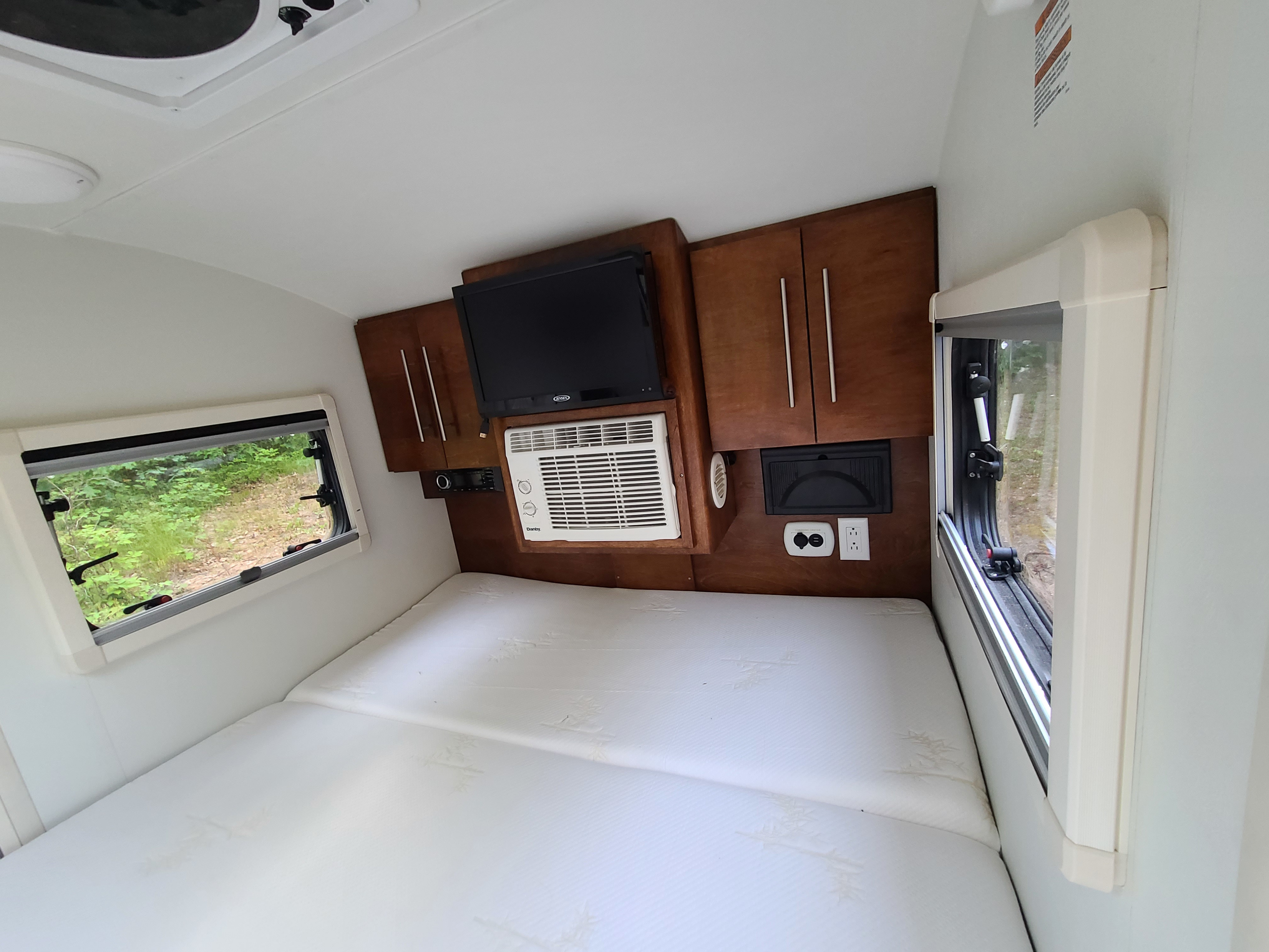 RV rental interior with a plush bed, TV, AC, wooden cabinets, and scenic window views for comfortable travel.. Nucamp Tag 2018