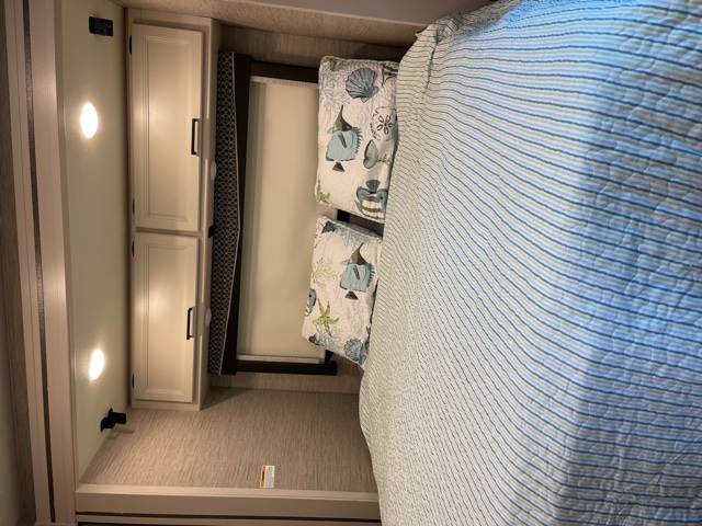 RV rental bedroom interior with a striped bed, sea-themed pillows, light cabinets, and wall lights, offering compact comfort.. Thor Motor Coach Gemini 2021