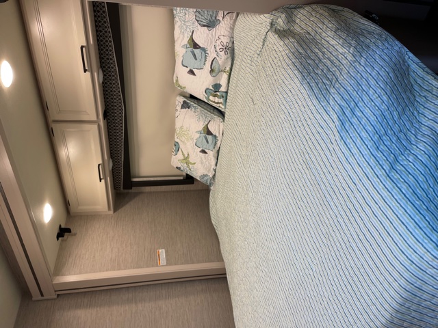 RV rental's cozy bedroom, featuring a neatly made bed with striped covers, sea-themed pillows, and wall-mounted lights.. Thor Motor Coach Gemini 2021
