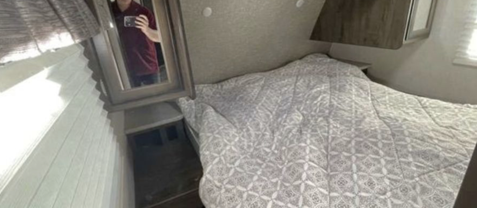 Compact RV rental bedroom showing a bed with patterned comforter, built-in mirror, and wall-mounted shades.. Heartland Mallard M26 2019