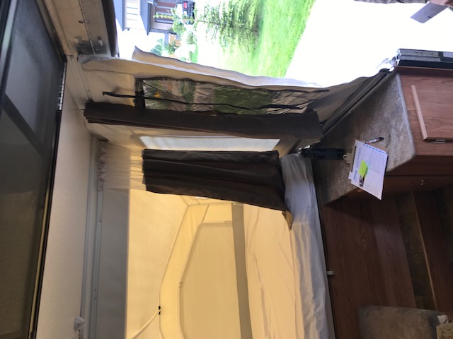 Interior of an RV rental pop-up camper: bed area with window insulation, dark curtains, and an adjacent counter.. Forest River 1940 LTD 2018