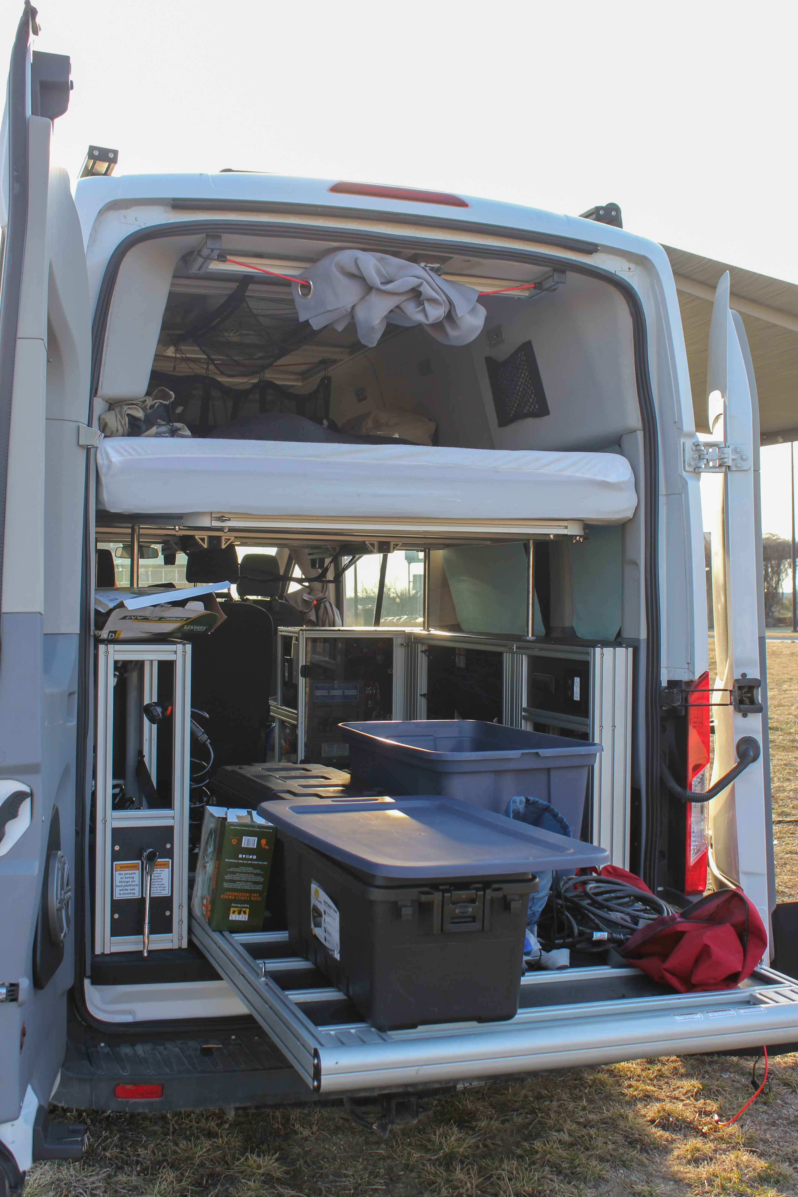 Inside an RV rental camper van, revealing a raised bed, organized storage, and a pull-out cargo platform with bins.. Ford Van 2017