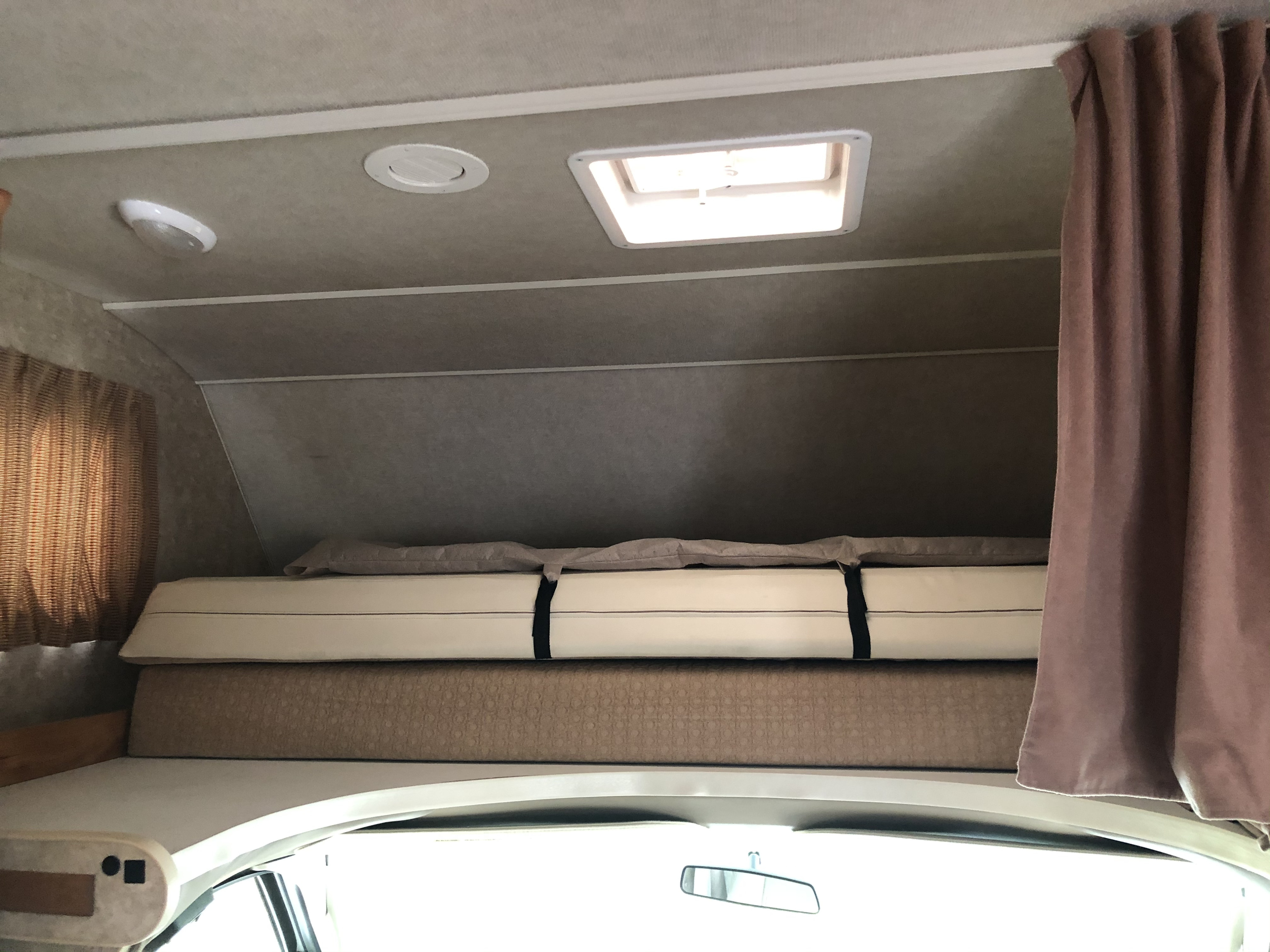 Cozy cab-over bunk in an RV rental, featuring a segmented mattress, ceiling lights, and a roof vent. Ready for travel.. Winnebago Chalet 2011