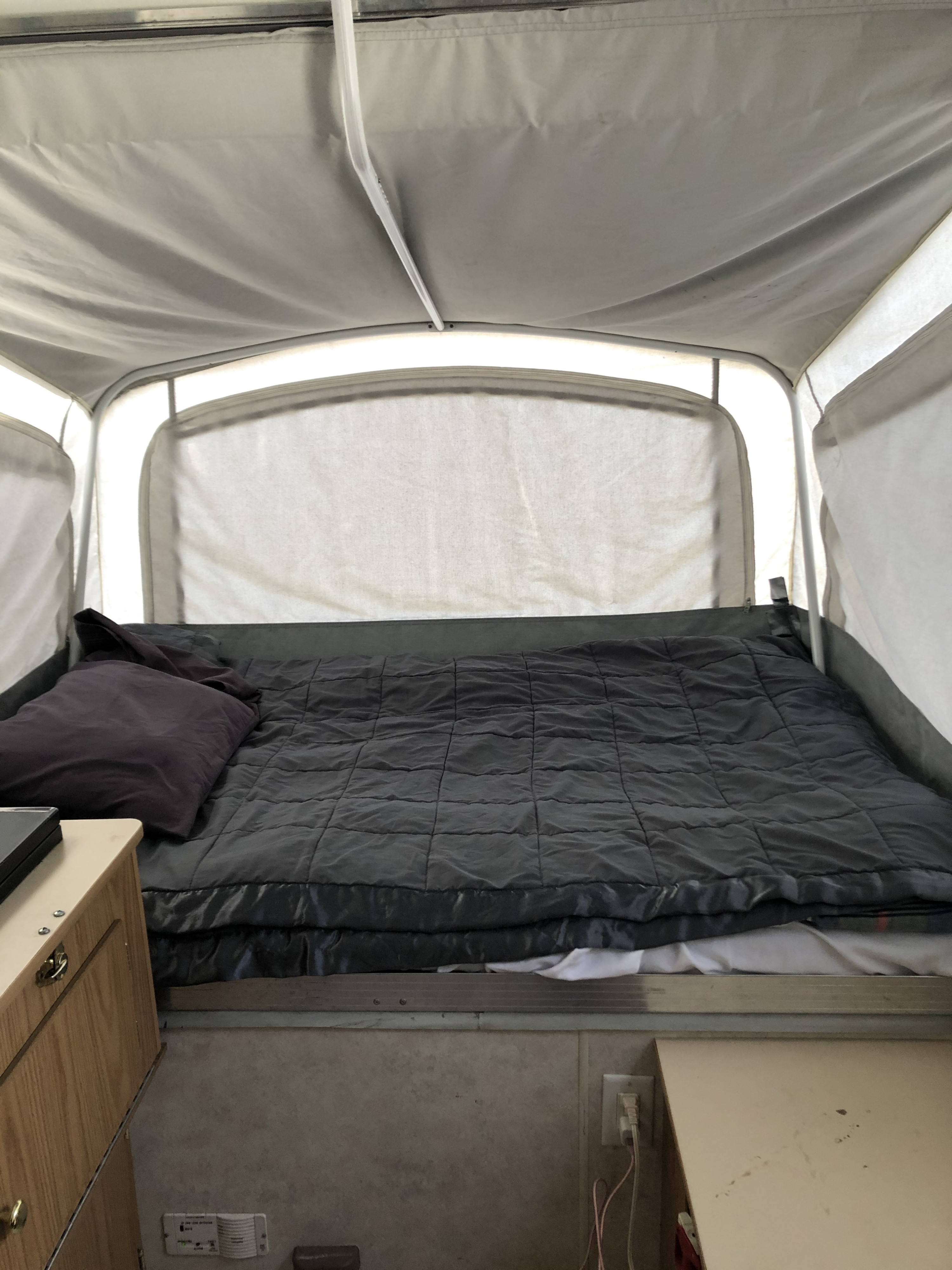 Comfortable sleeping area in an RV rental pop-up camper, featuring a dark bed and fabric walls.. Coleman Destiny Taos 1999