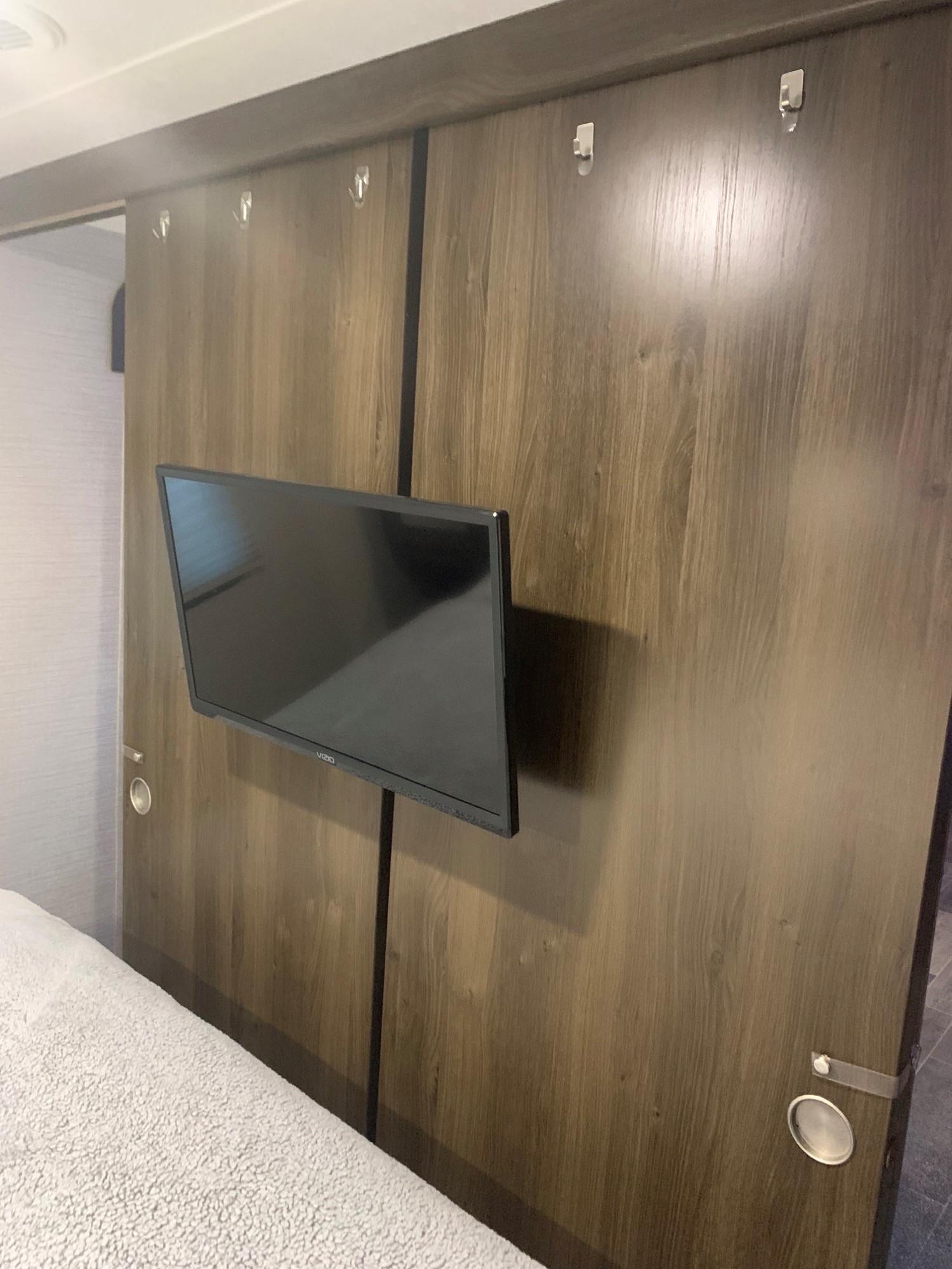 RV rental bedroom with a mounted TV, wood-grain sliding panel wall, hooks, and a bed in the foreground.. Keystone RV Bullet Ultra Lite 2018