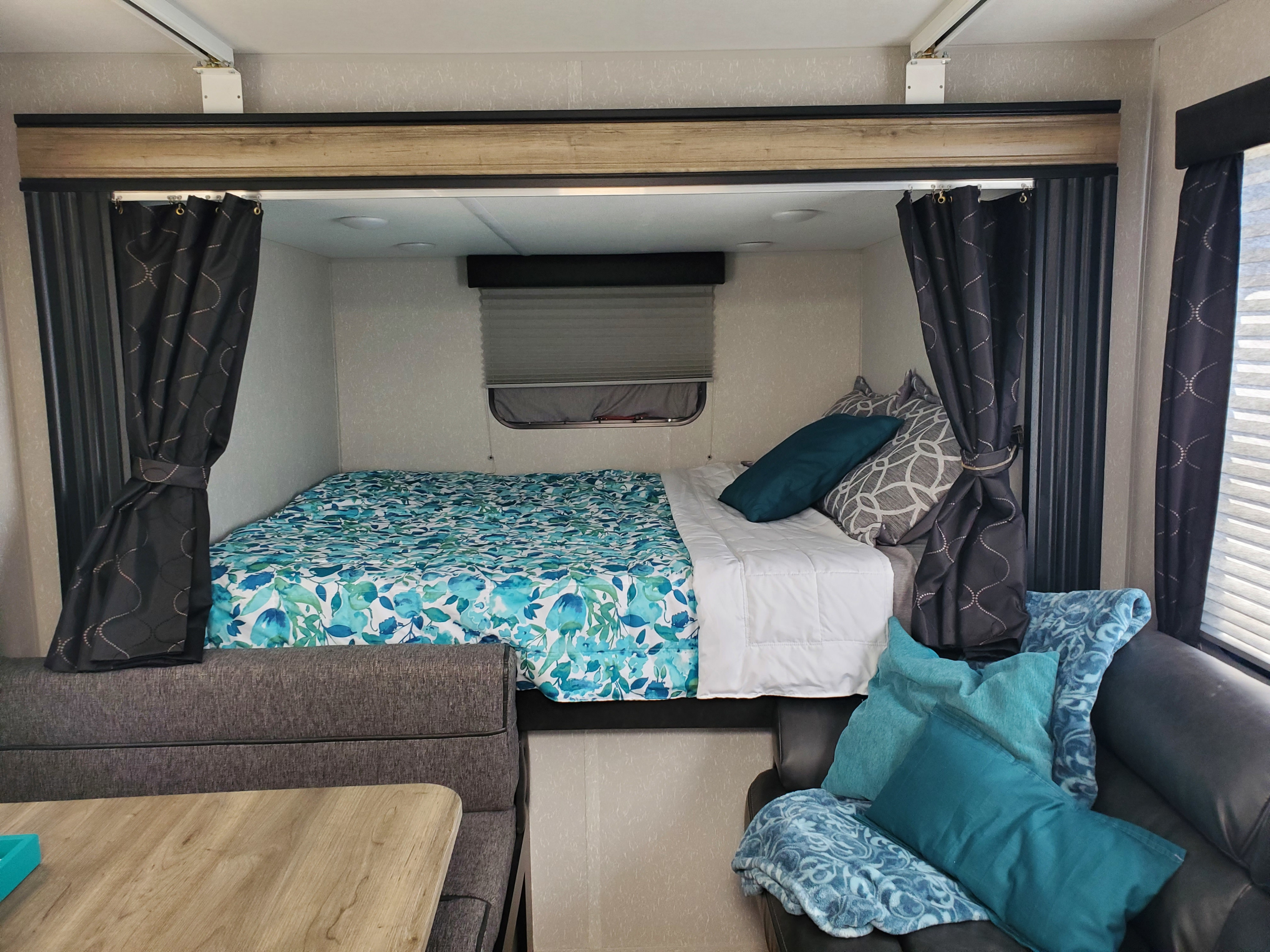 Inside a cozy RV rental: floral bed, window, and inviting seating area with blue and gray accents.. Forest River Cherokee Grey Wolf 2021