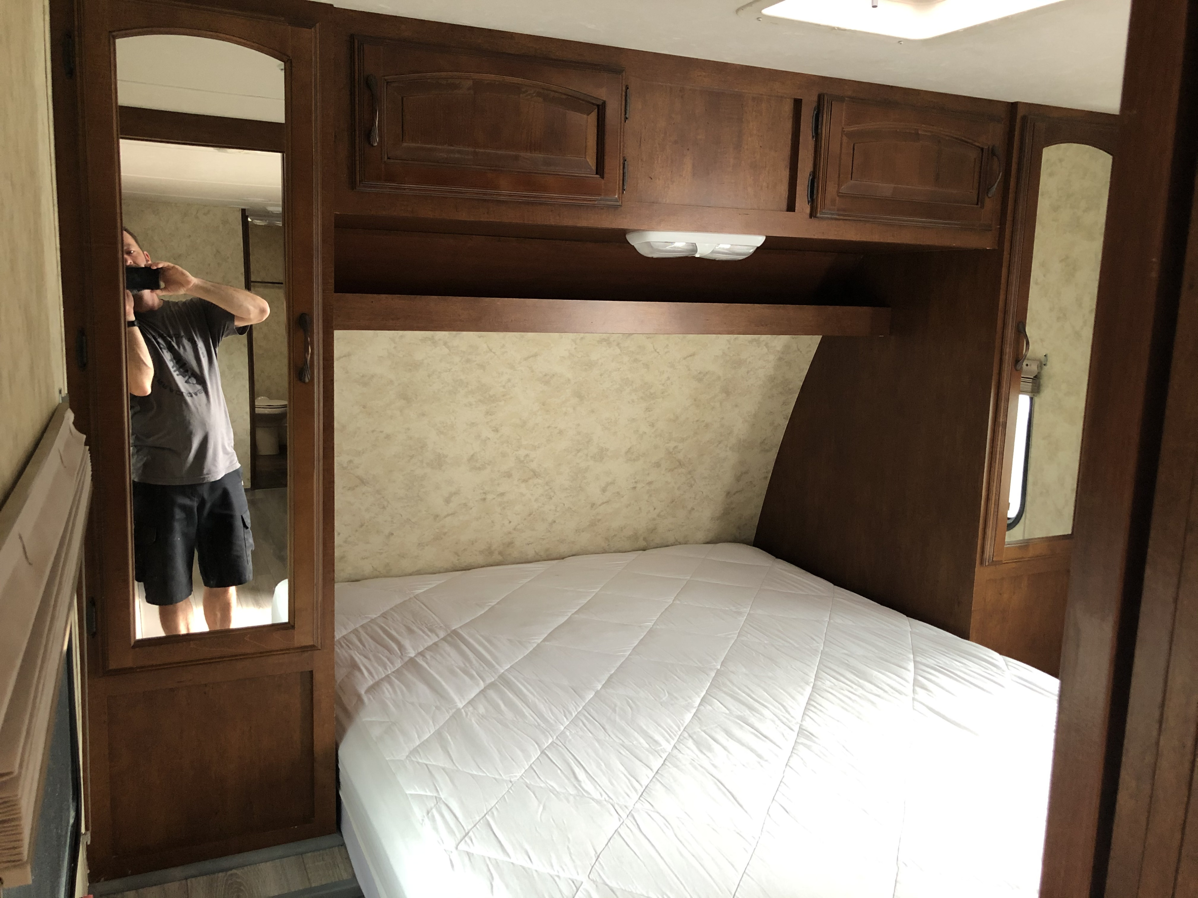 This RV rental's bedroom interior features a bed with white bedding, wooden overhead cabinets, and a mirrored wardrobe on the left.. Coachmen Chaparral 2011