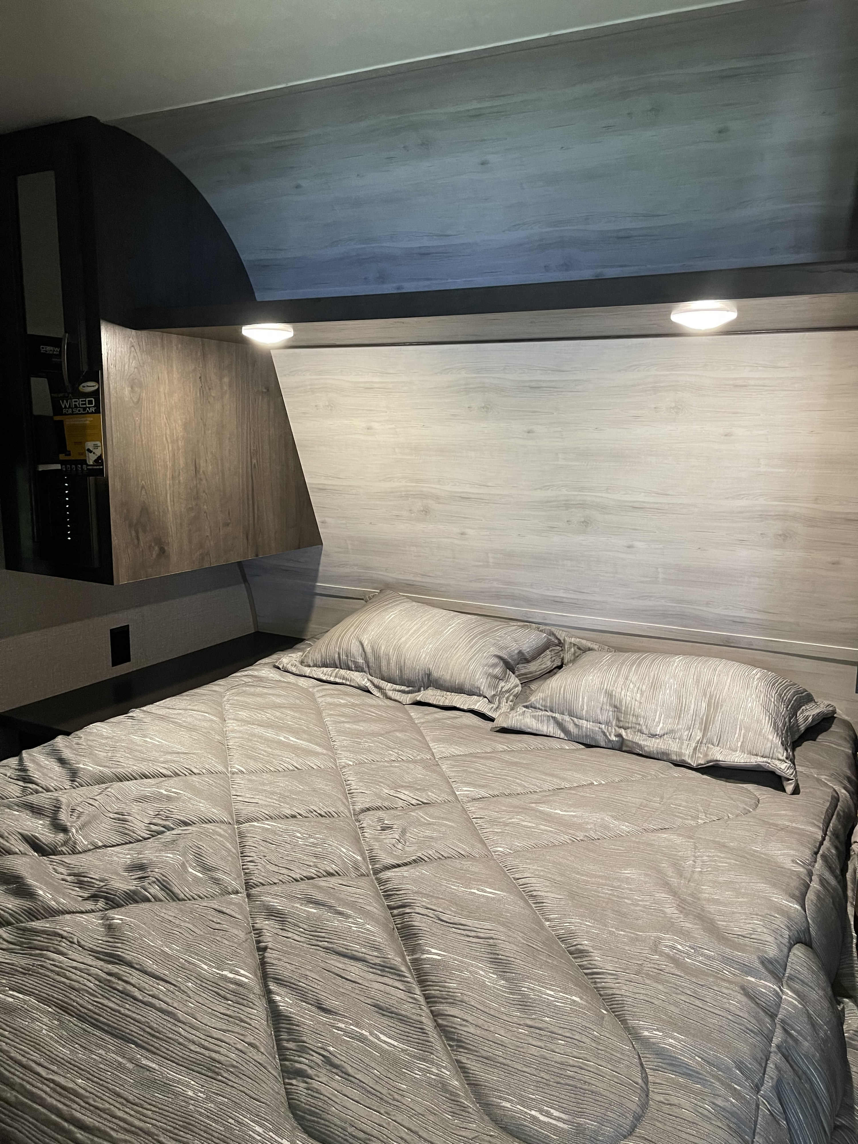 Cozy RV rental bedroom with a grey textured bed, two pillows, and built-in reading lights. 'WIRED FOR SOLAR' panel visible on left.. Jayco Jay Flight Swift 2021