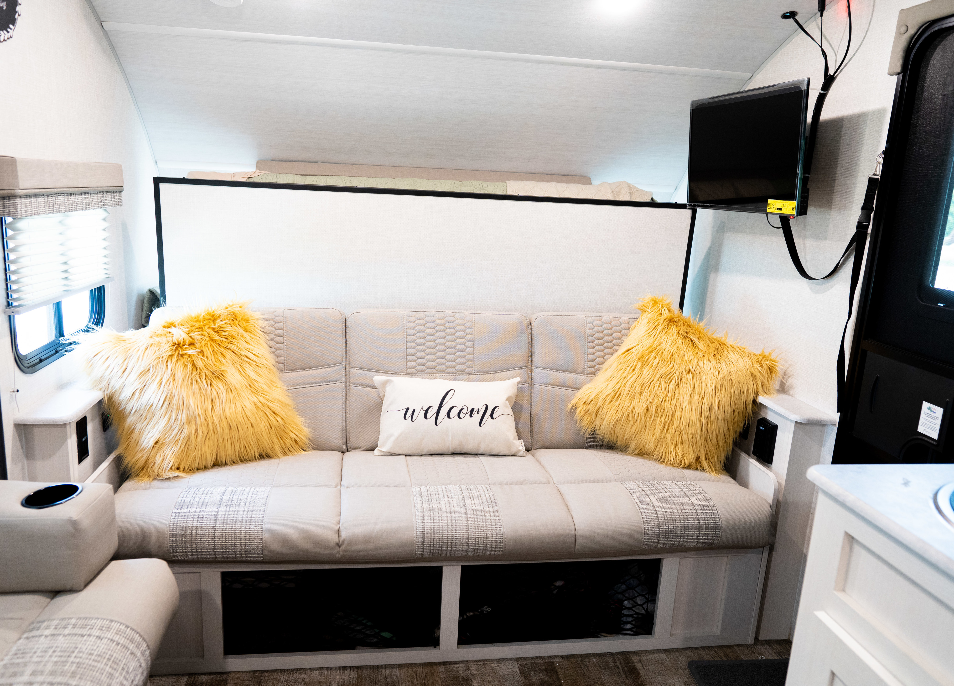 Step inside this modern **RV rental**! Features a comfy sofa with fuzzy pillows, 'welcome' pillow, overhead bunk, and mounted TV.. Forest River R-Pod 2021