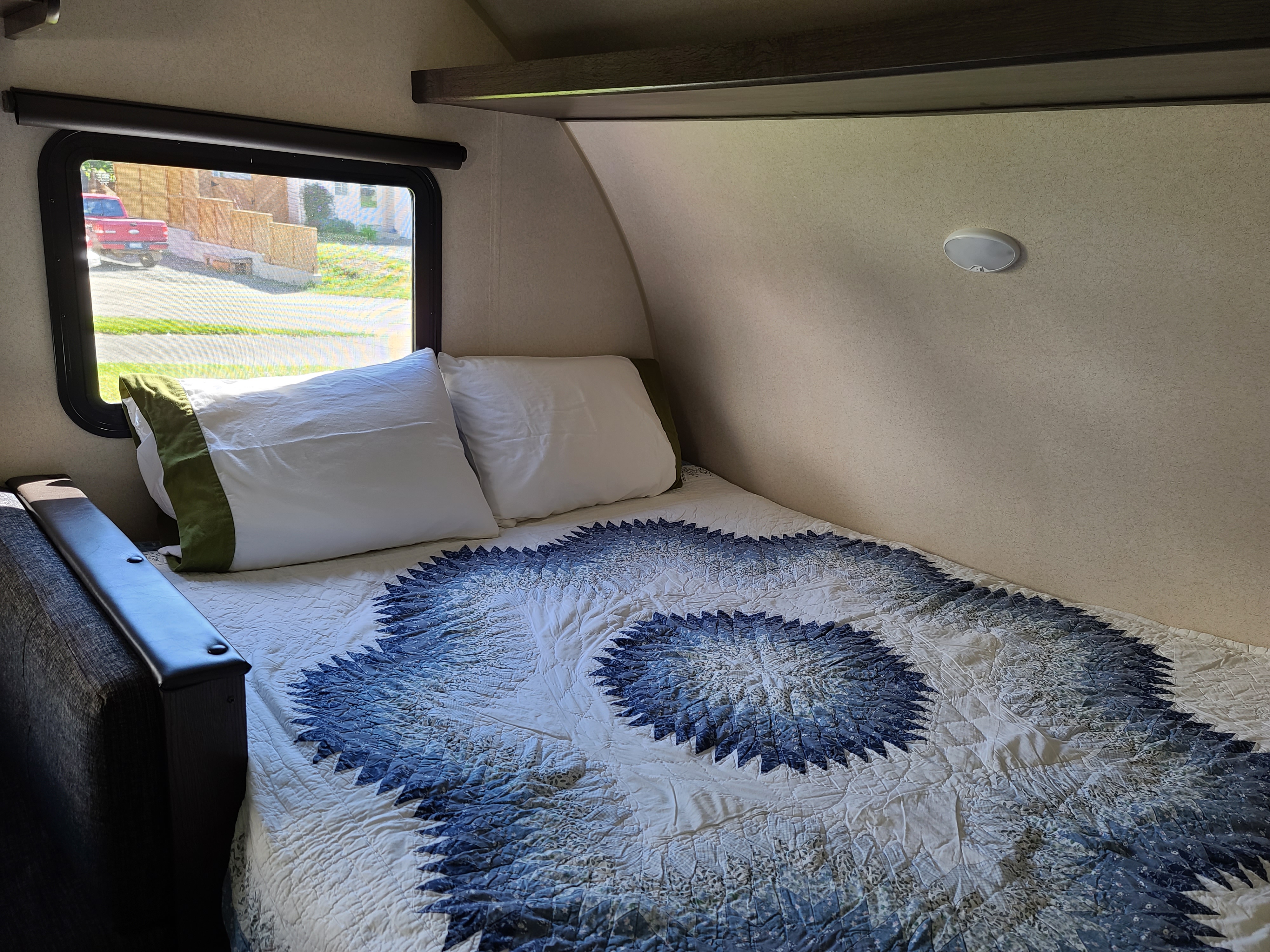 Cozy RV rental interior features a bed with a unique blue quilt, pillows, window view, and compact shelving.. Forest River Salem 2019