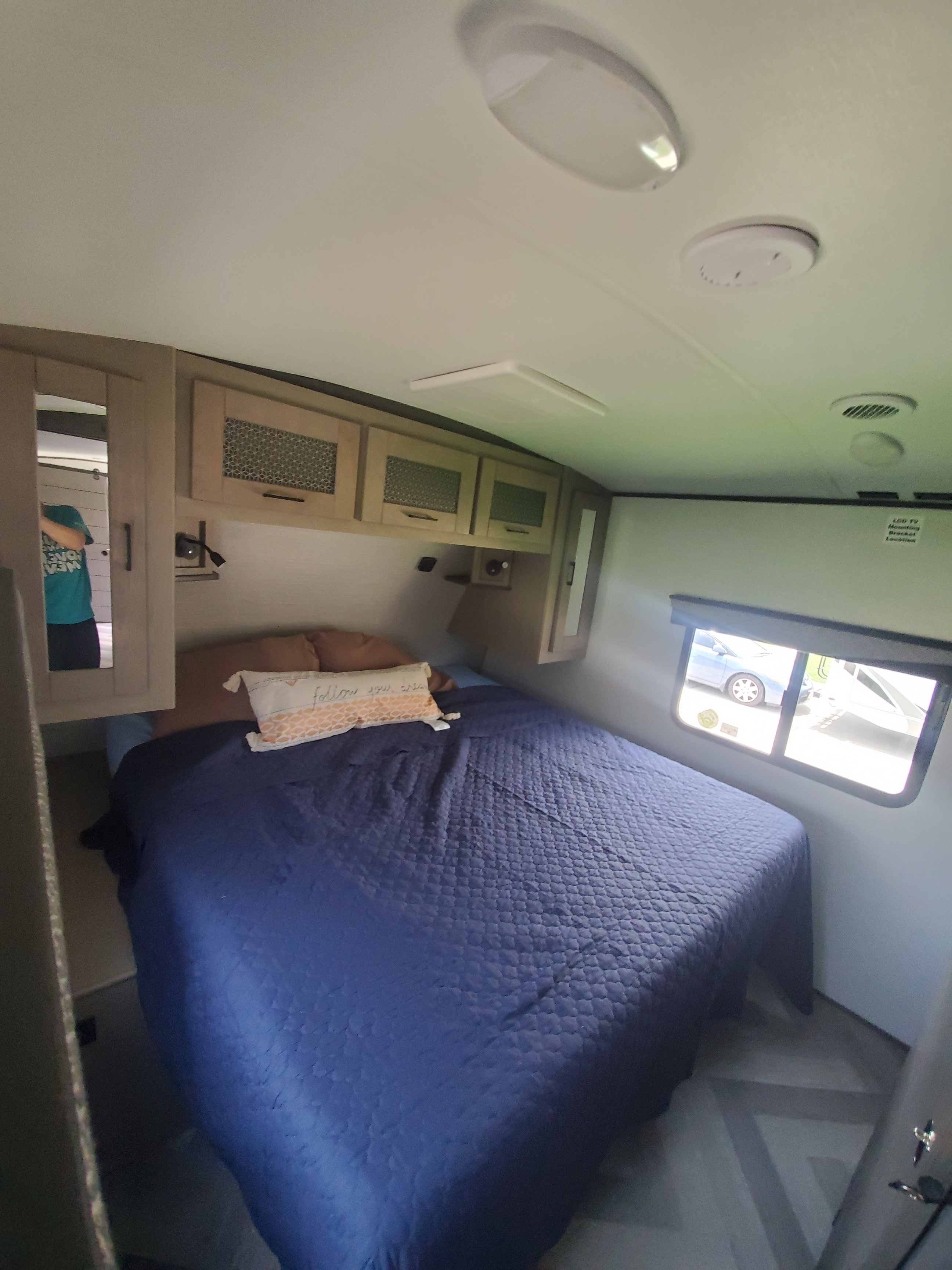 Cozy RV rental bedroom: blue quilted bed, overhead cabinets, and a bright window looking outside.. Cruiser Rv Corp Cruiser 2021