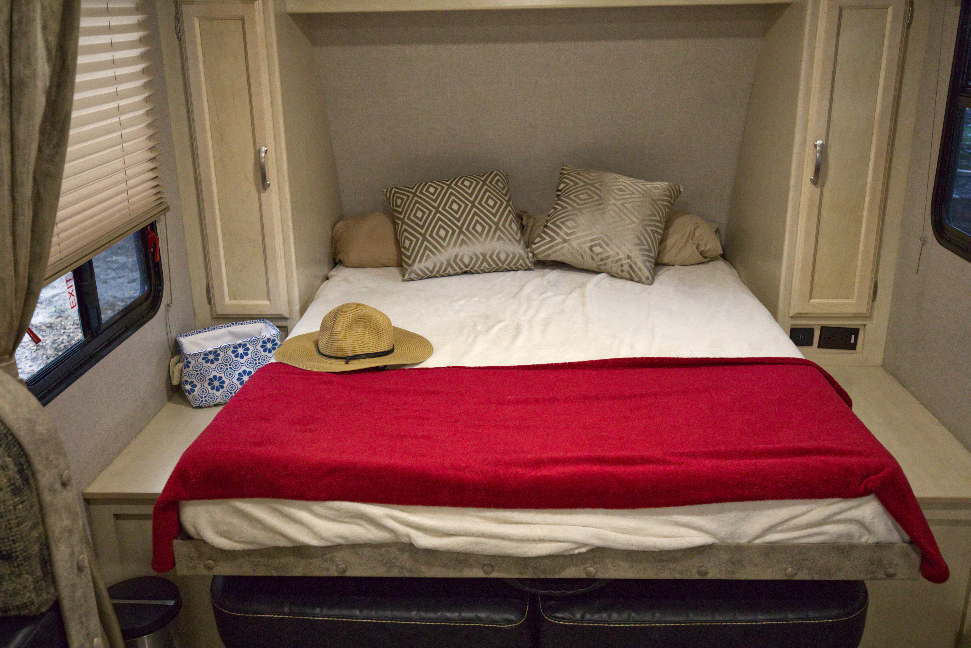 Comfortable RV rental bedroom setup with a bed, red blanket, decorative pillows, and essential power outlets.. Other Other 2019