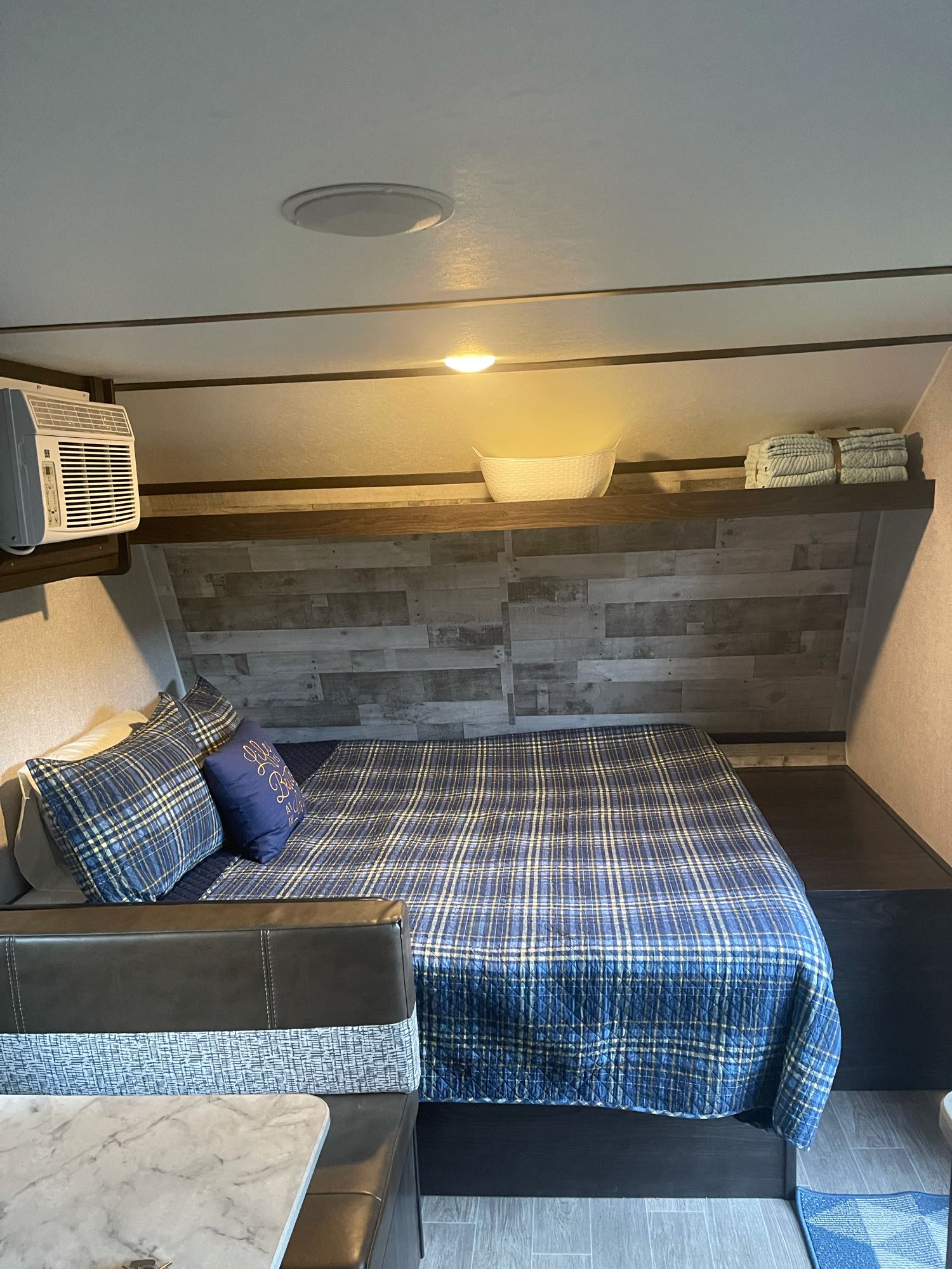 Cozy RV rental bedroom features a blue plaid bed, AC, wooden accent wall, and useful shelf space.. Dutchmen Coleman 2021