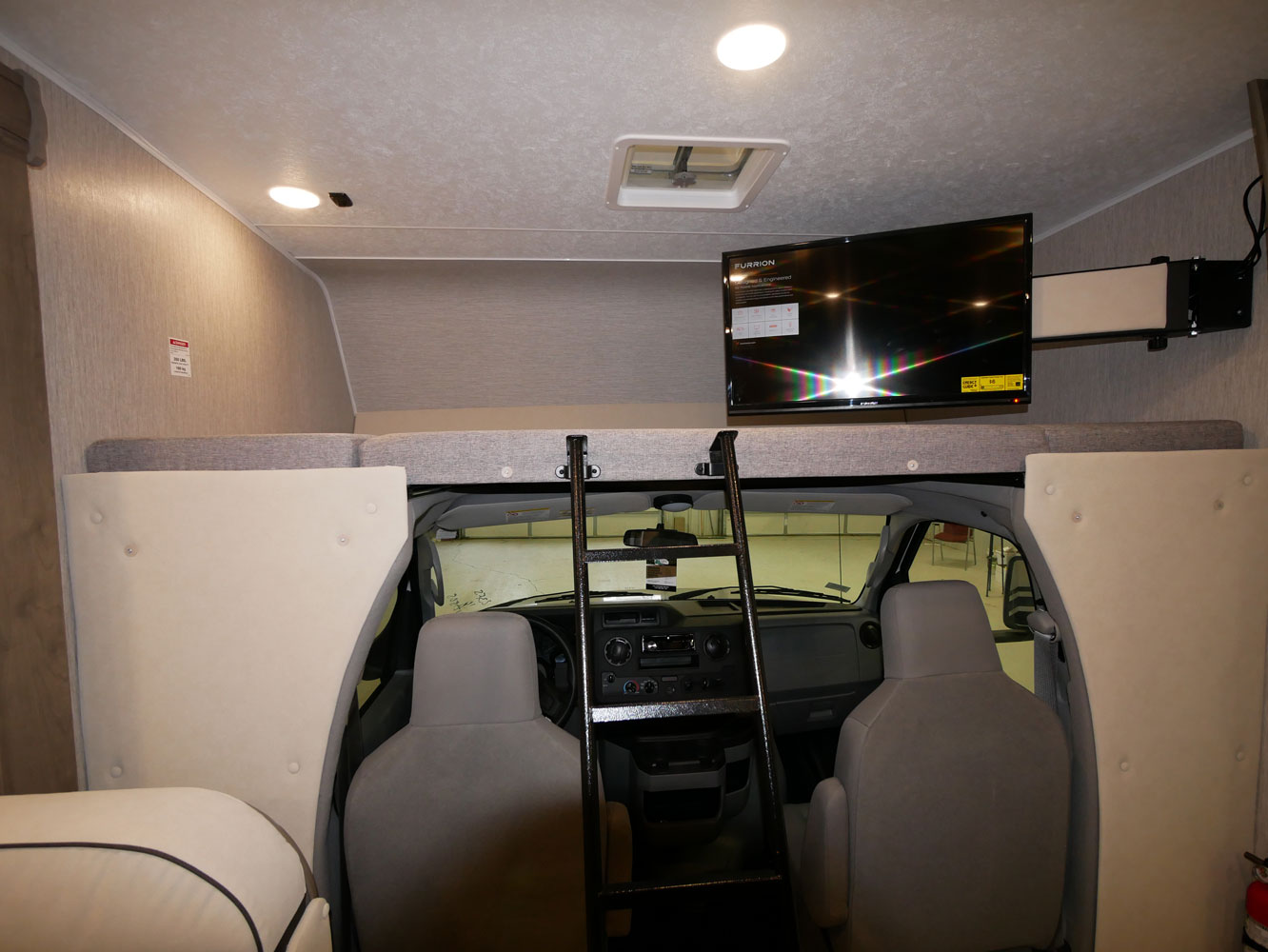 Inside an RV rental: view of the cockpit, over-cab bunk with ladder, and TV, offering a cozy travel living space.. Coachmen Freelander 23FS 2022