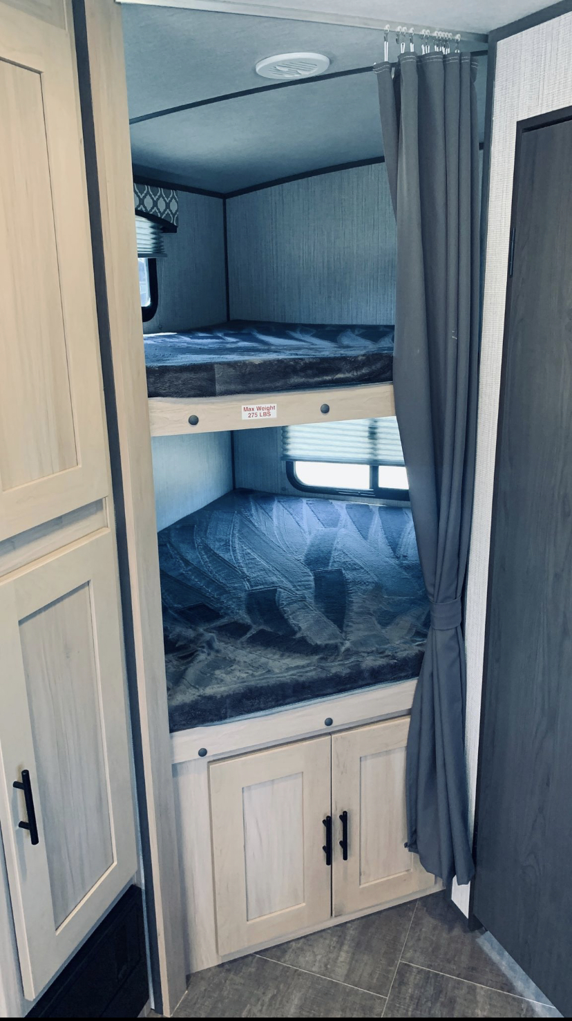RV rental interior showcasing cozy bunk beds with soft blankets, a window, and storage cabinets, plus a privacy curtain.. Crusier RV Corp radiance 2021