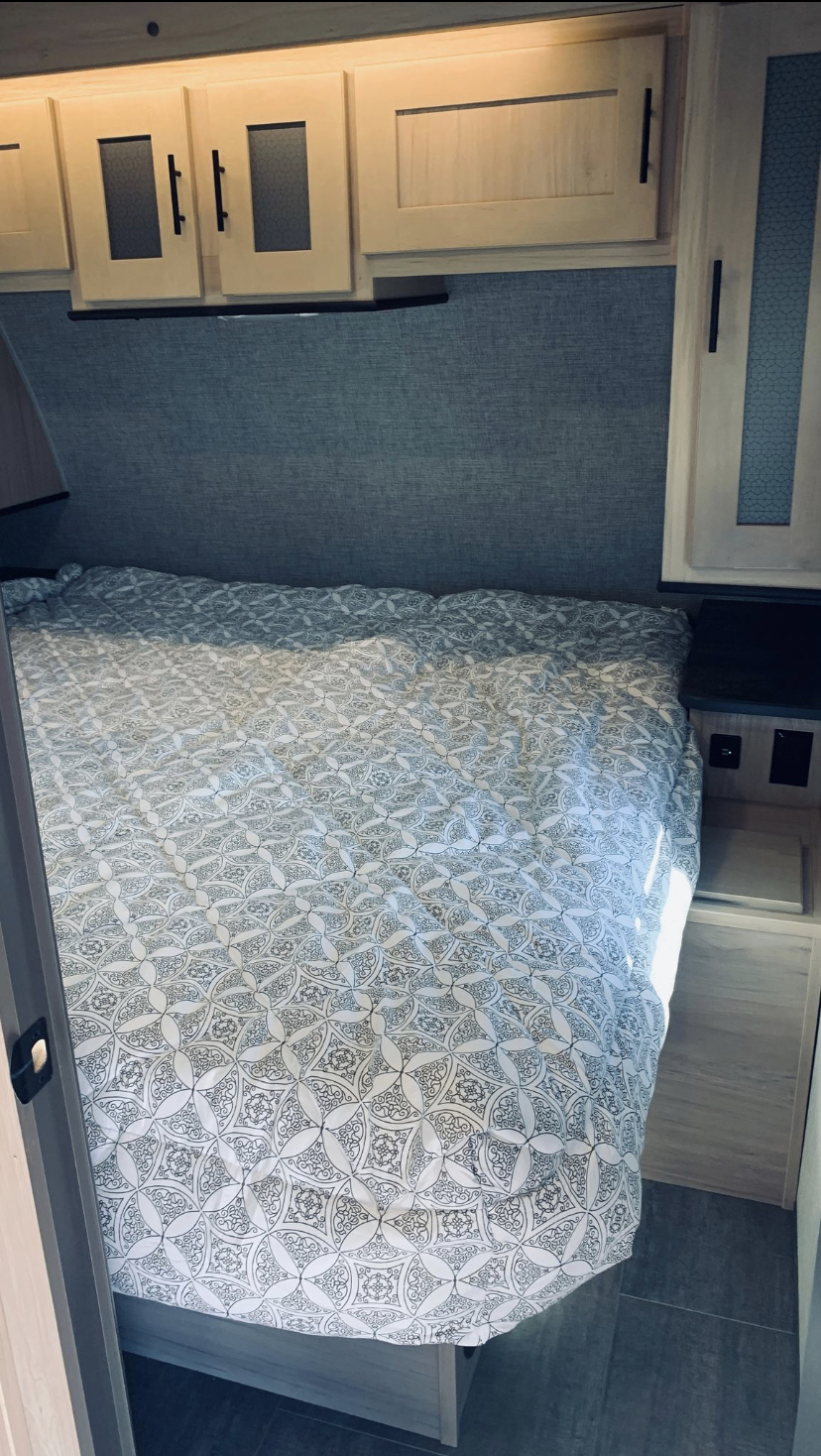 Inside a comfortable RV rental bedroom, featuring a patterned bed, overhead cabinets, and compact bedside table.. Crusier RV Corp radiance 2021