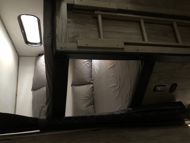 Cozy rv rental bunk bed area with gray bedding, an attached ladder, and a bright oval window providing light.. Forest River Cherokee Alpha Wolf 2021
