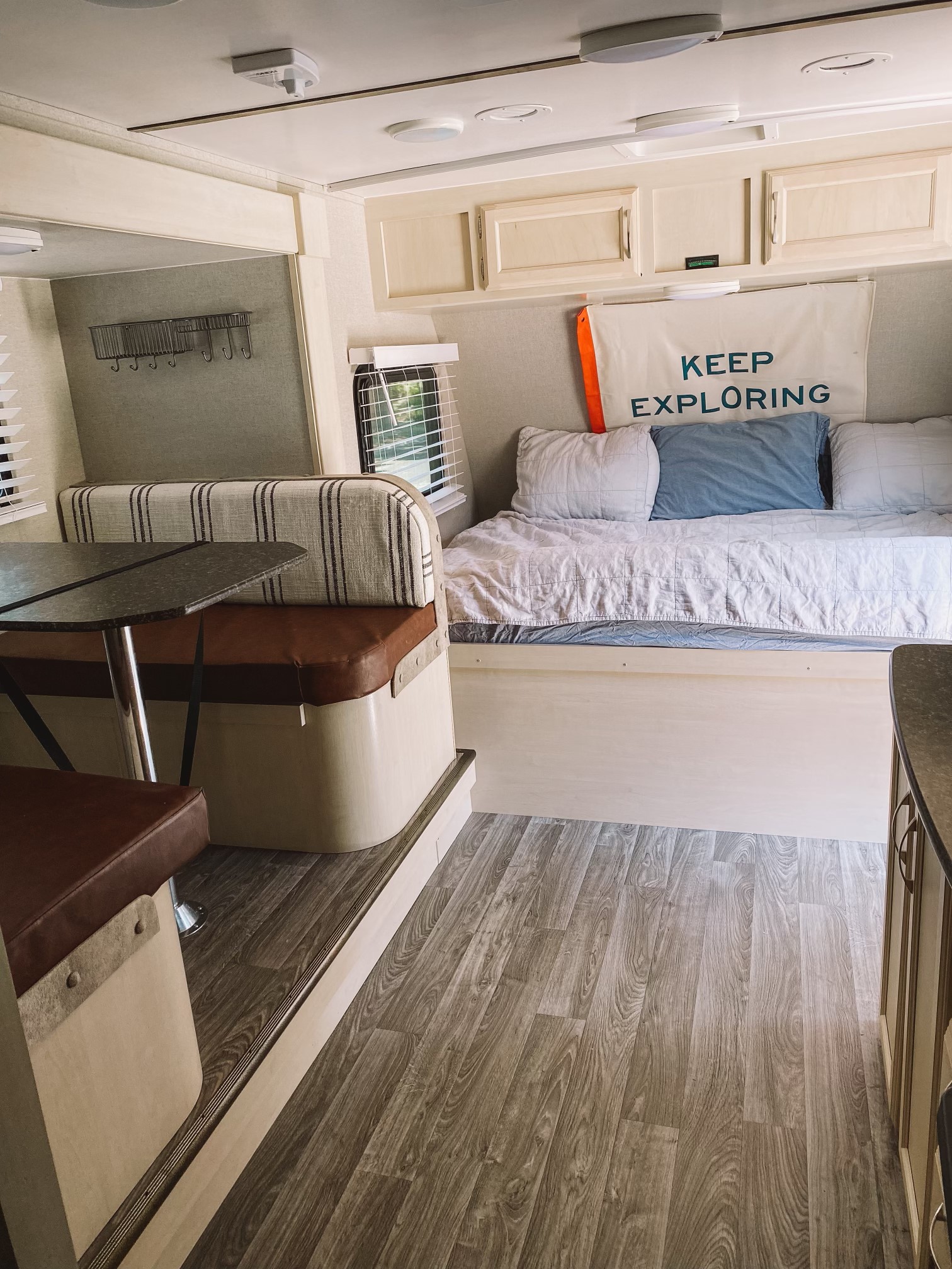Step into this bright RV rental interior, showcasing a dining booth, comfy bed, overhead cabinets, and wood-look flooring.. Winnebago Micro Minnie 2019