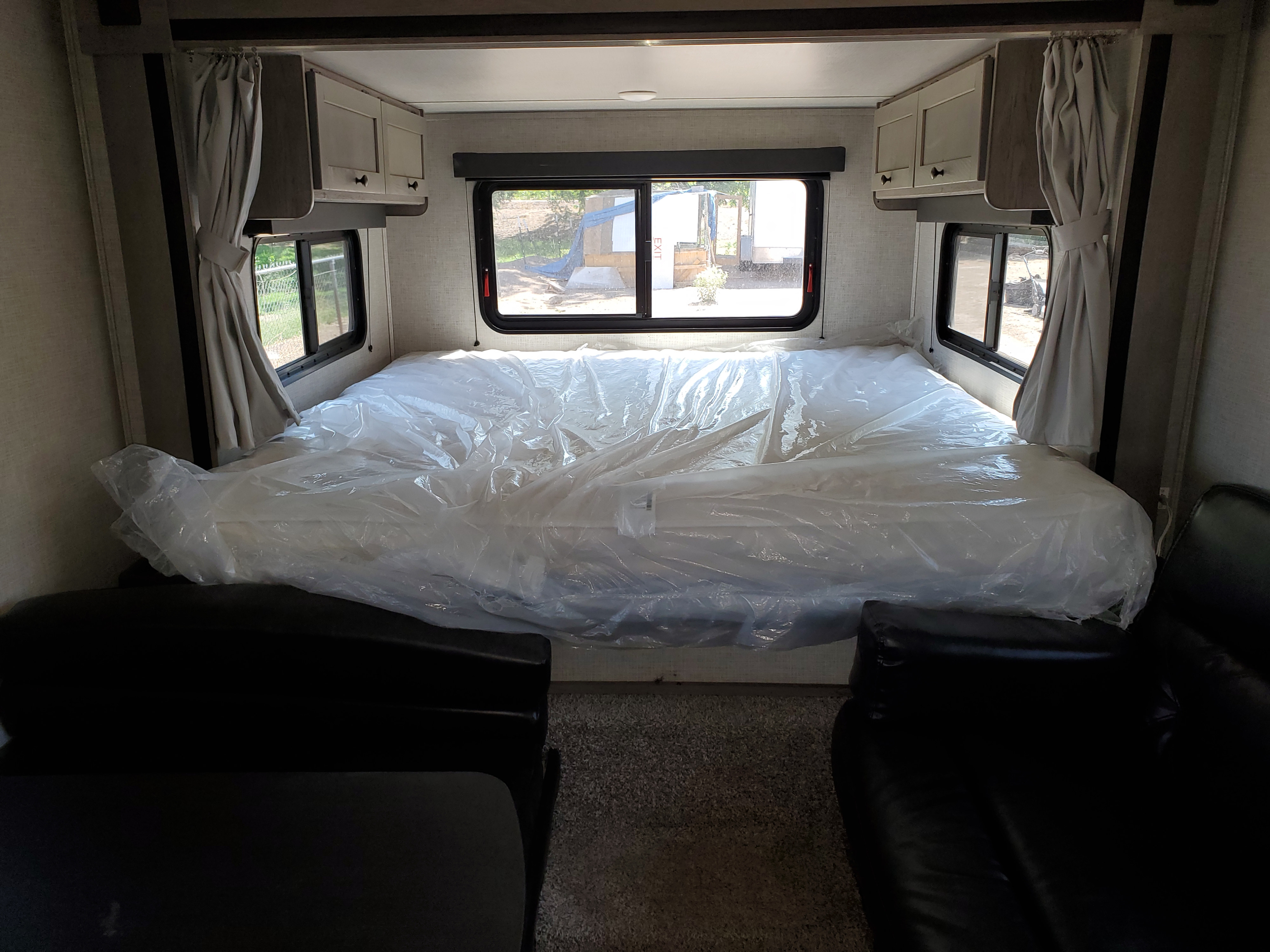 Clean RV rental bedroom featuring a new, plastic-wrapped mattress, overhead cabinets, and bright windows on both sides.. Keystone Outback 2020