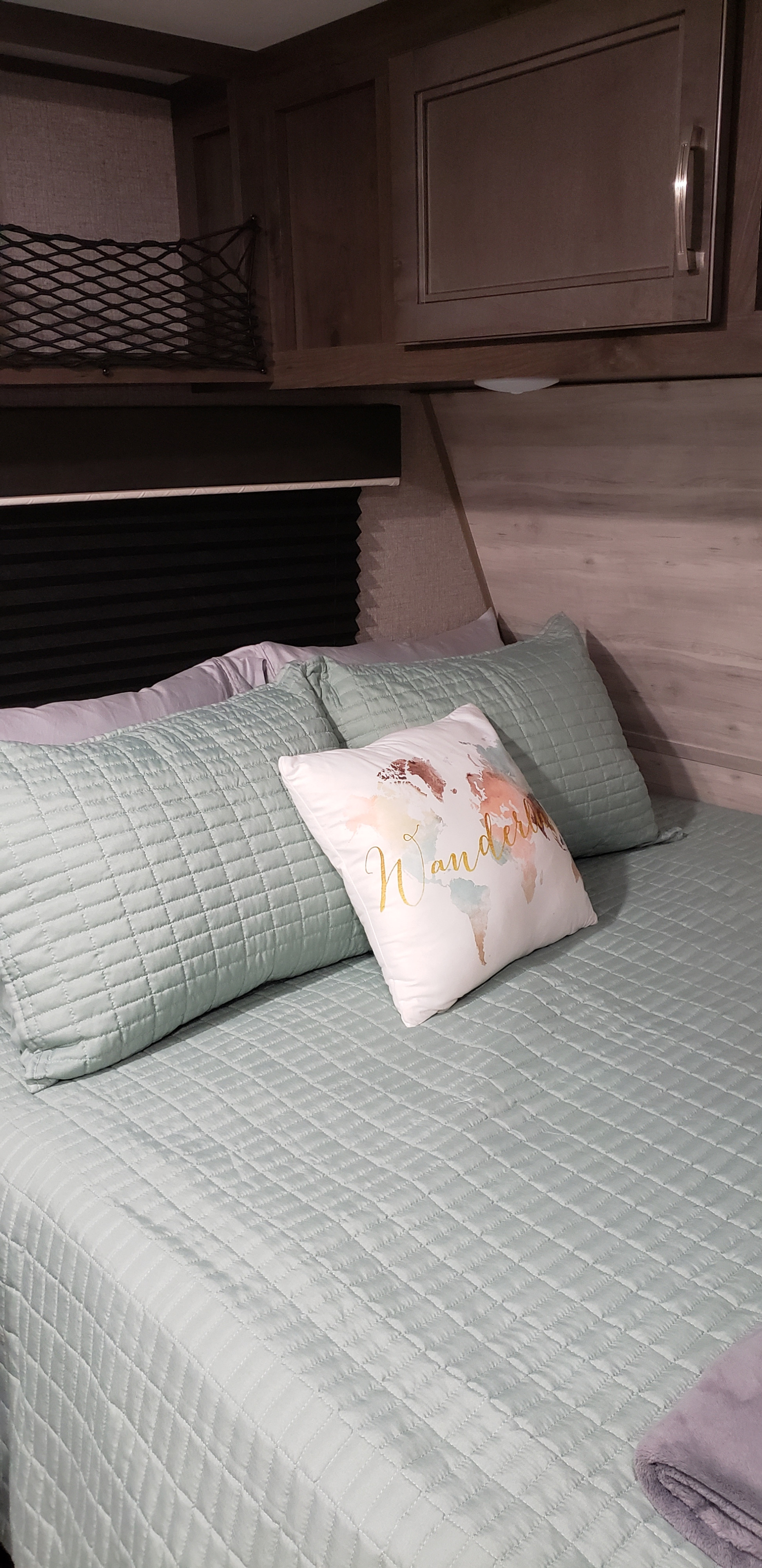 Cozy RV rental bedroom with light green quilted bedding, 'Wander' pillow, and overhead storage. Perfect for your next trip.. Jayco Jay Flight 2021