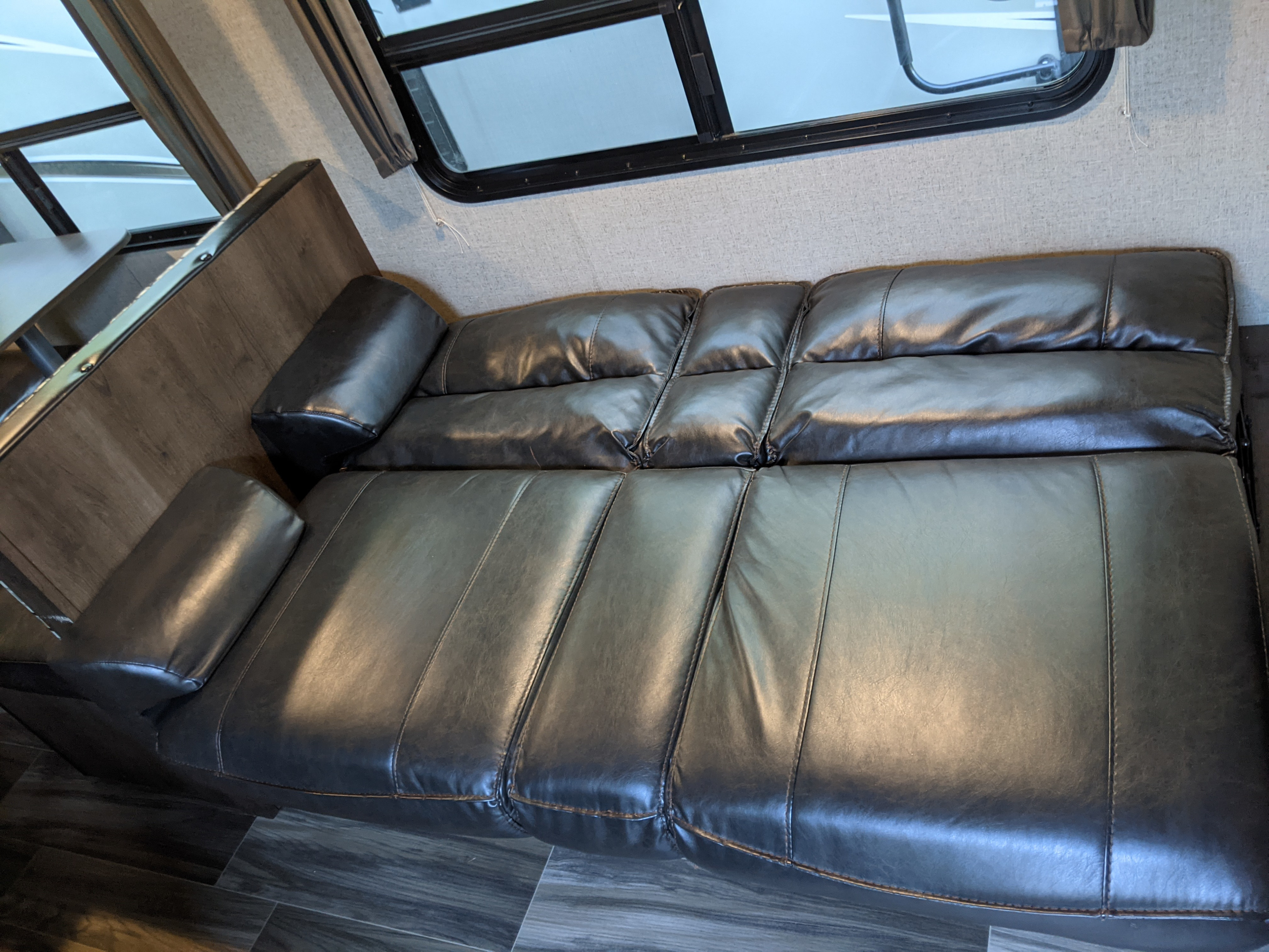 Spacious, dark faux-leather sofa in an RV rental, converting to a bed for comfortable rest and travel lodging.. Shasta Oasis 2019