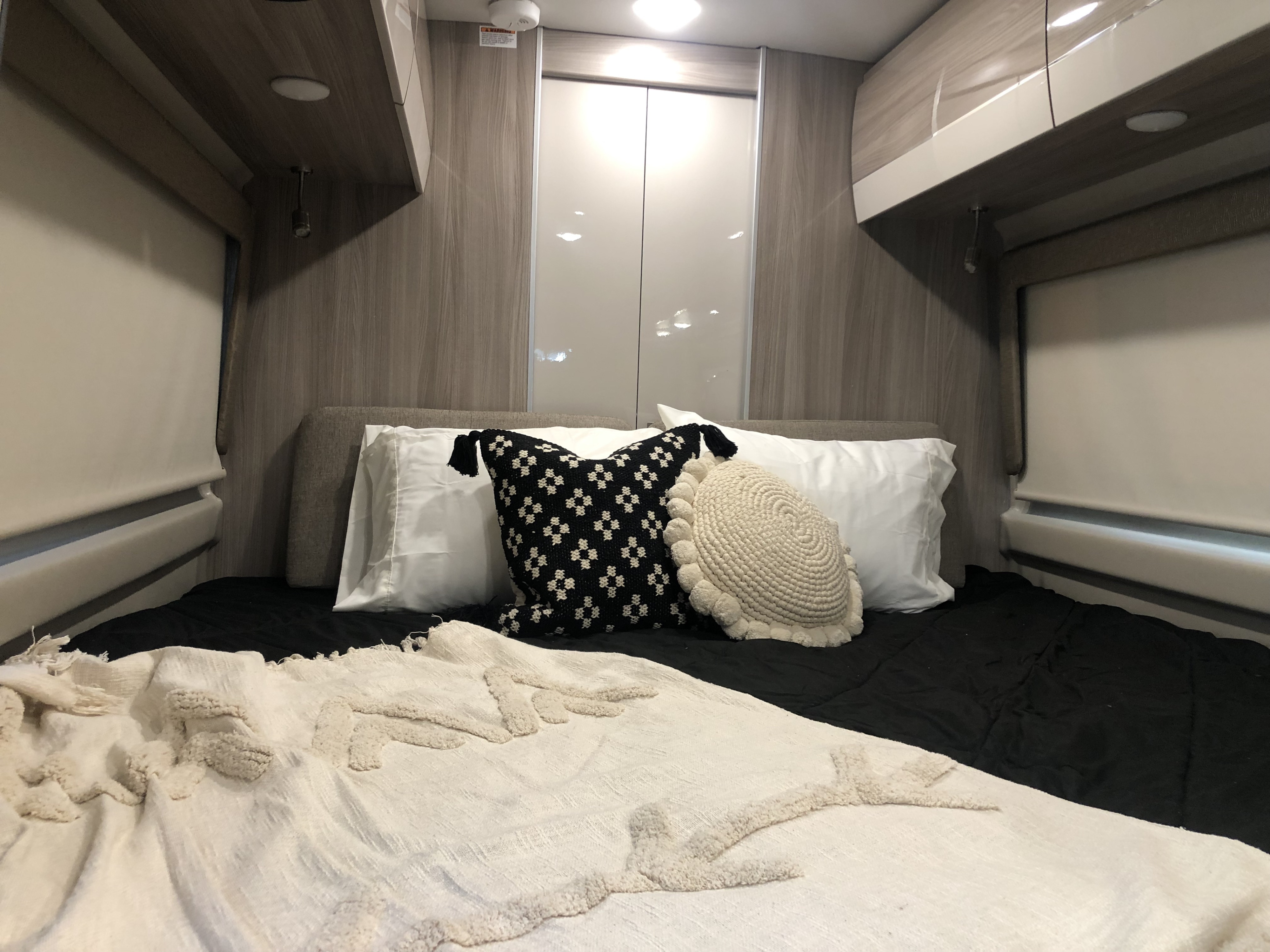 Cozy RV rental bedroom with a black bed, white patterned pillows, textured throw, and modern wood-toned interior.. Thor Sequence 2021