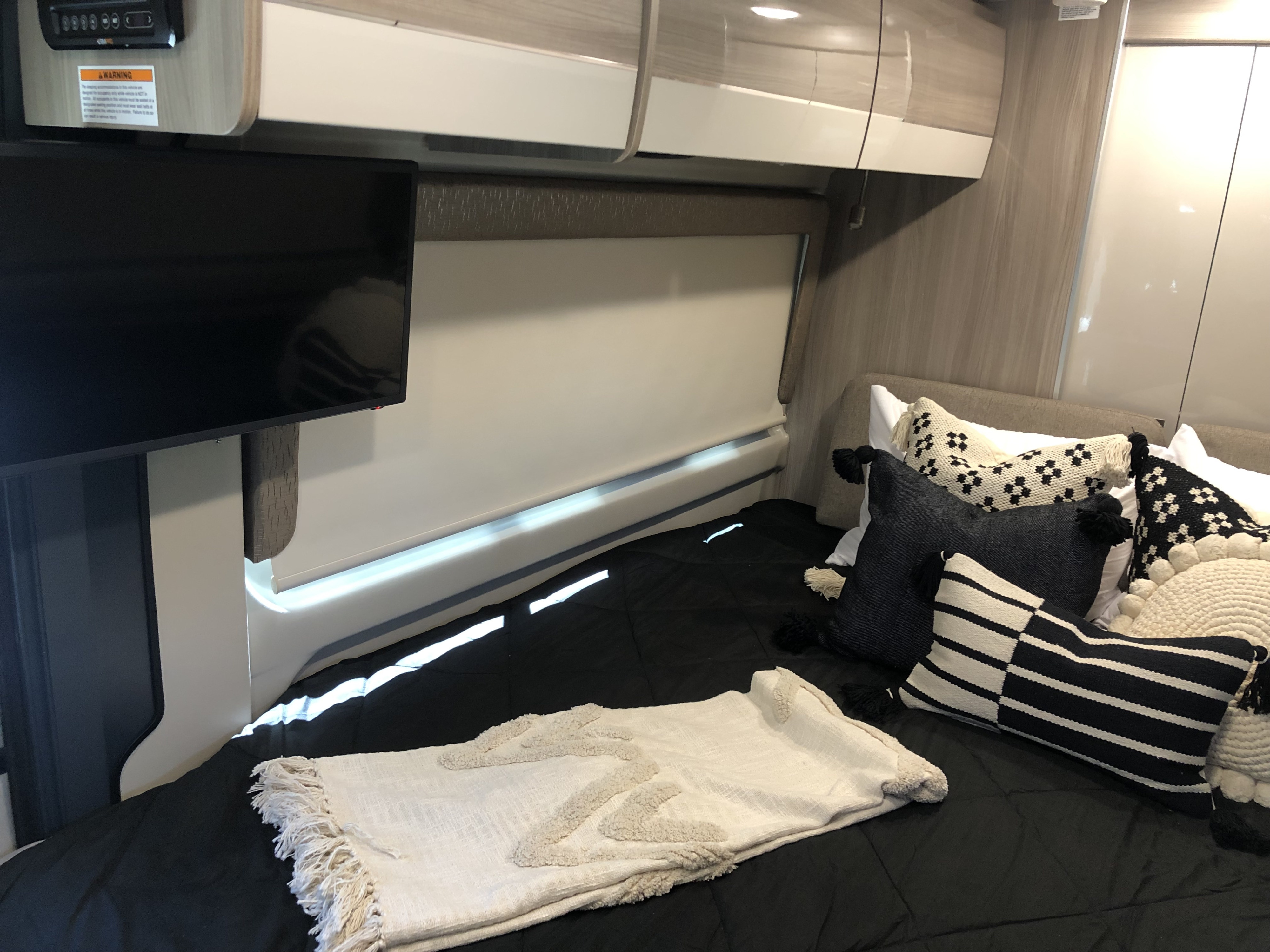 Cozy RV rental bedroom with TV, plush pillows, and overhead storage for a comfortable journey.. Thor Sequence 2021