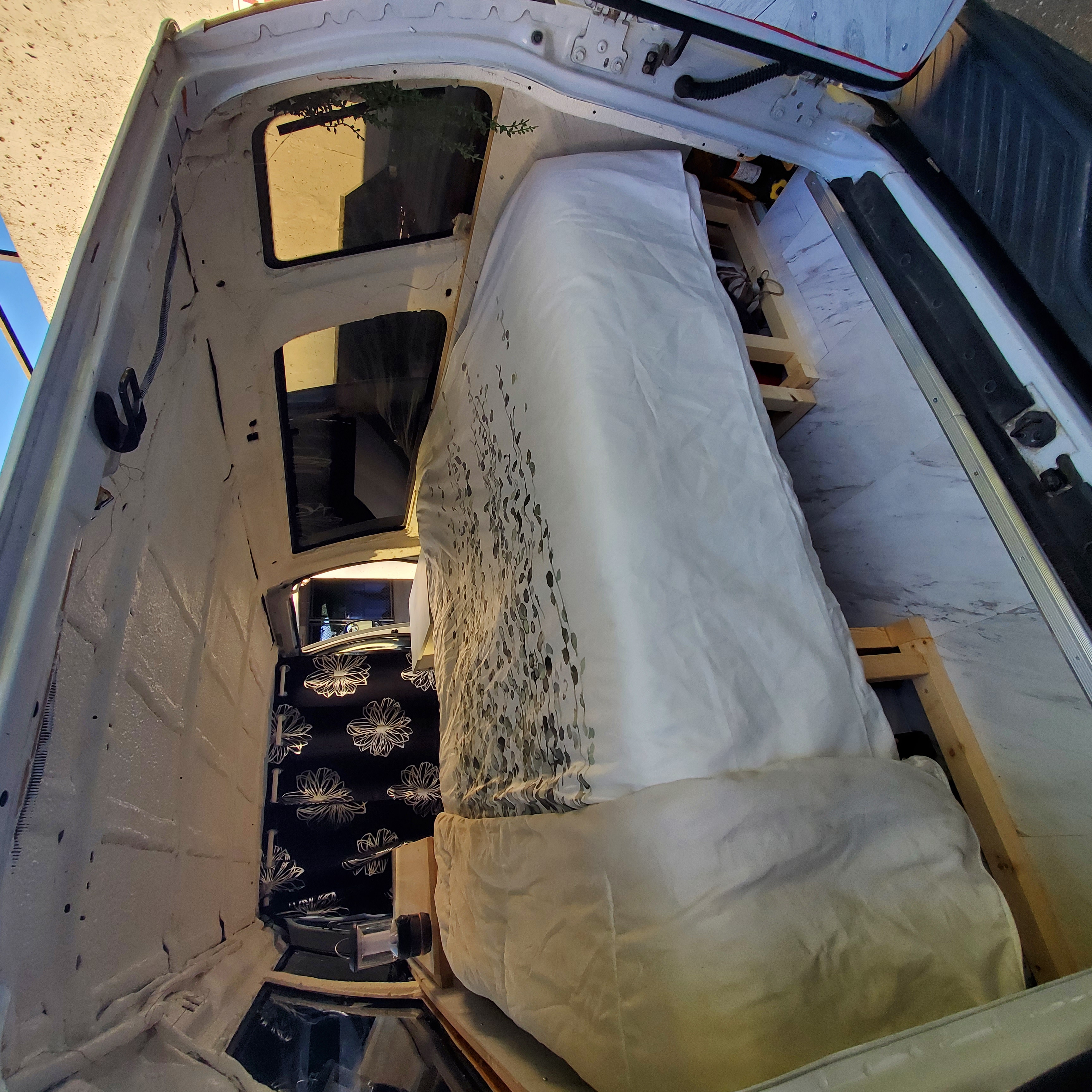 RV rental van interior: A neatly converted space with a bed, white bedding on a wooden frame & insulated walls.. Ford Econoline Club Wagon 2011