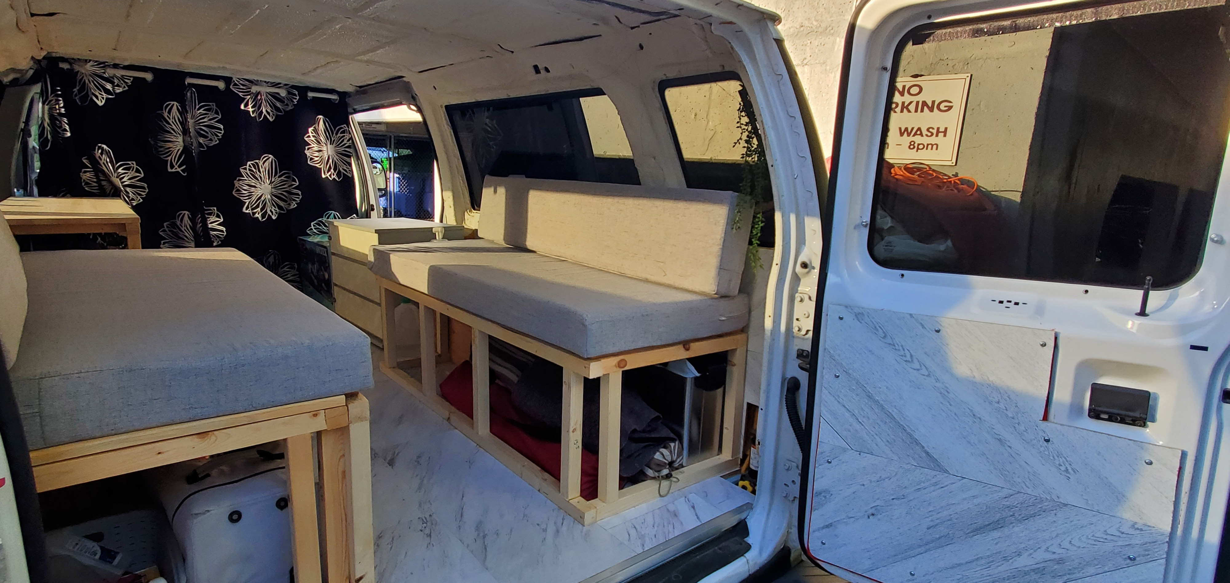 Interior of a small RV rental, featuring grey cushioned benches, under-seat storage, and floral curtains, offering a cozy travel space.. Ford Econoline Club Wagon 2011