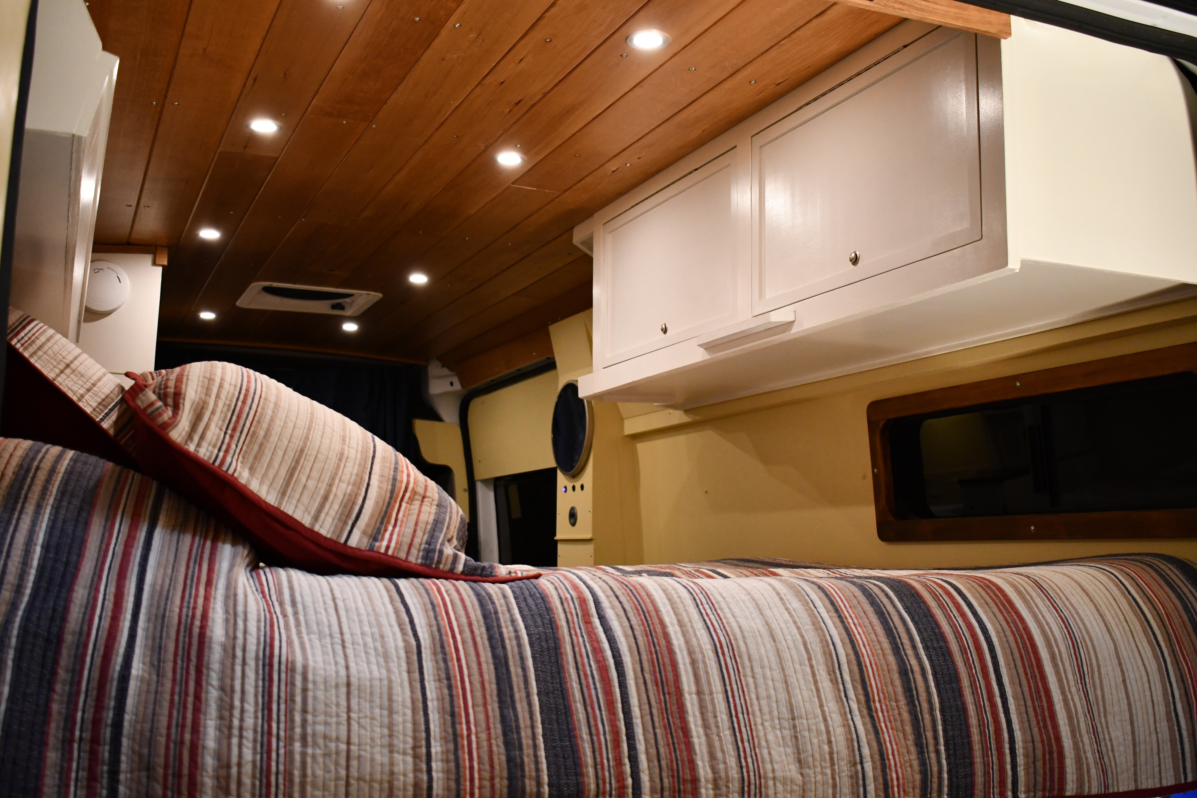 Cozy RV rental interior showcasing a bed with striped bedding, overhead cabinets, and a warm wooden ceiling.. Other Other 2021