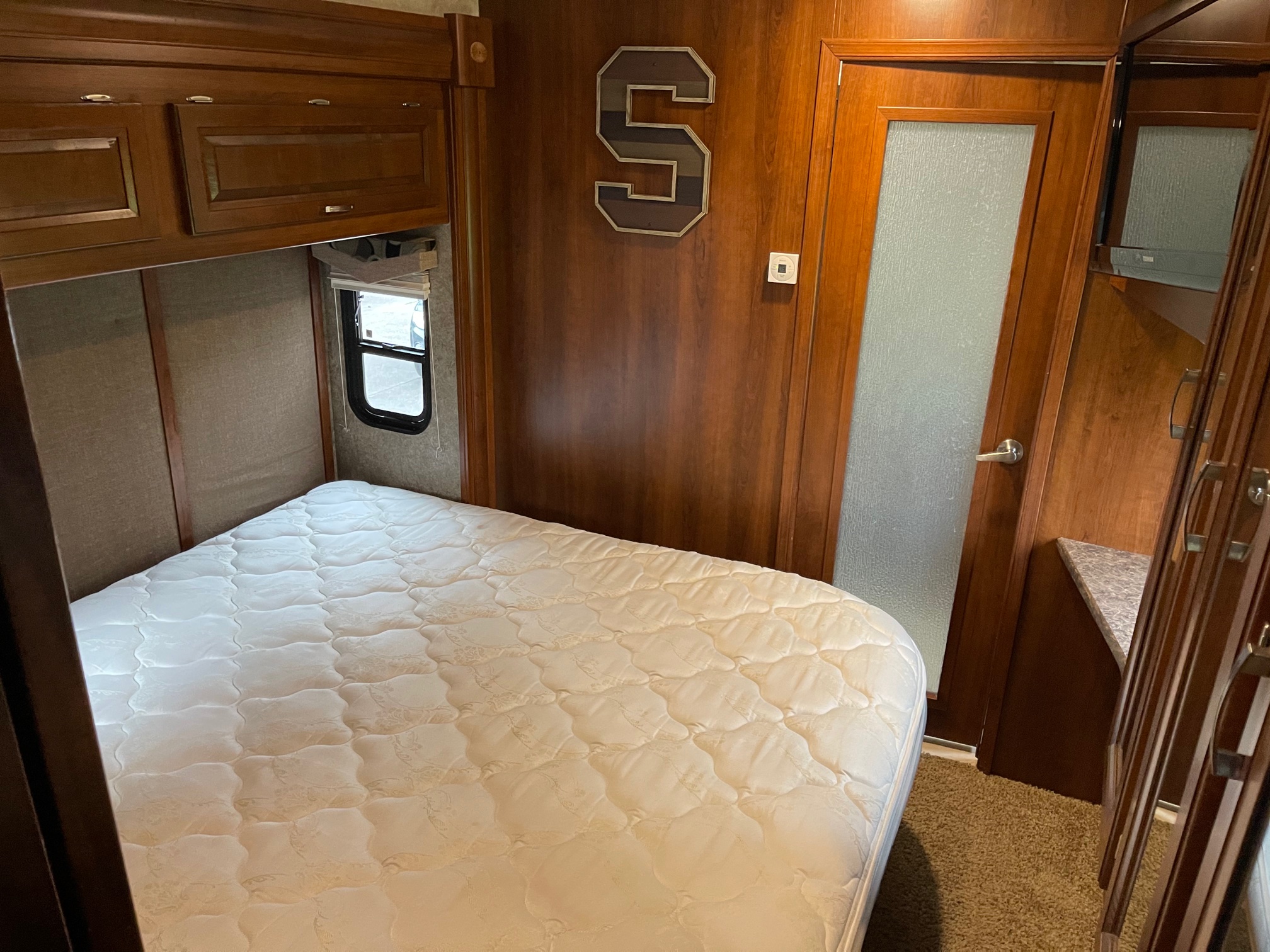 Cozy RV rental bedroom showing a comfortable bed, overhead storage, and frosted glass door, perfect for travel accommodations.. Forest River Georgetown 2013