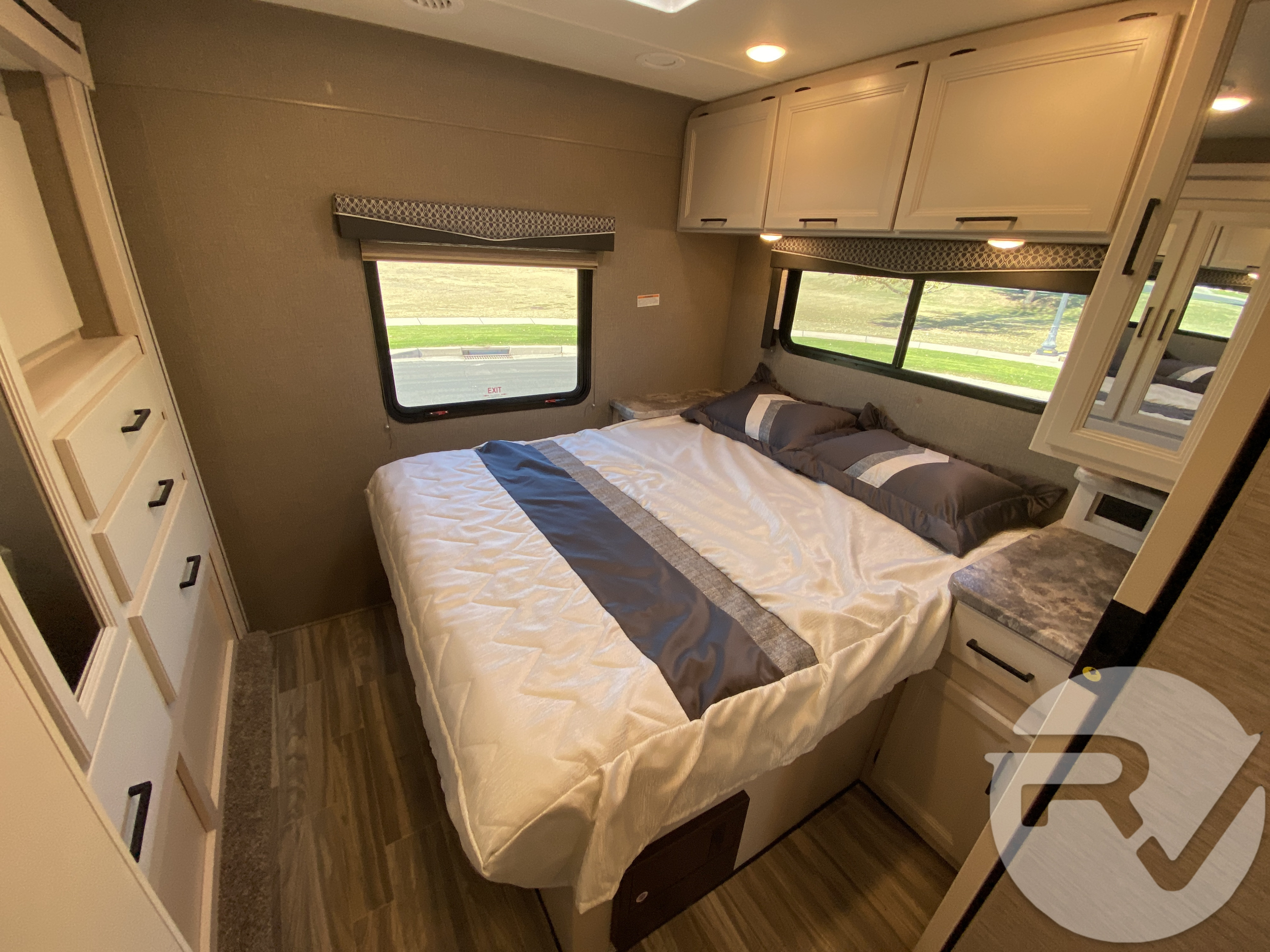 Cozy RV rental bedroom featuring a queen bed with gray bedding, overhead cabinets, and built-in storage.. Thor Motor Coach Four Winds 2021