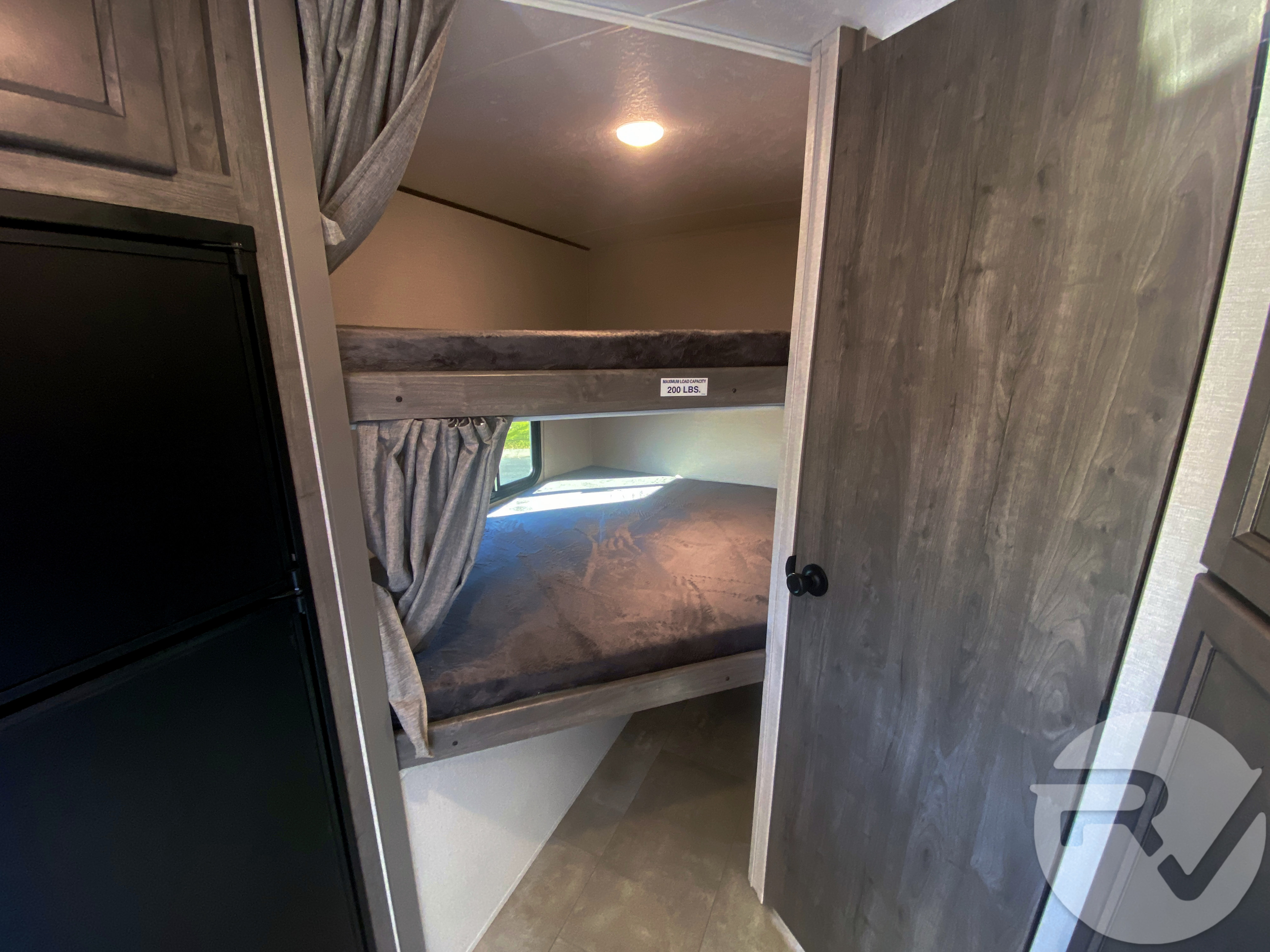 RV rental interior featuring cozy bunk beds with privacy curtains, a refrigerator, and stylish wood-grain cabinetry.. Coachmen Apex 2021