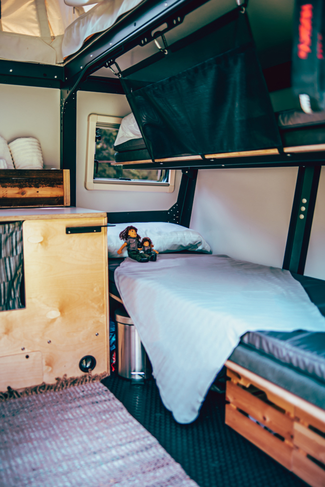 Cozy bunk beds inside this RV rental's compact sleeping area, with storage and a window view.. TAXA Outdoors Mantis Camper 2020
