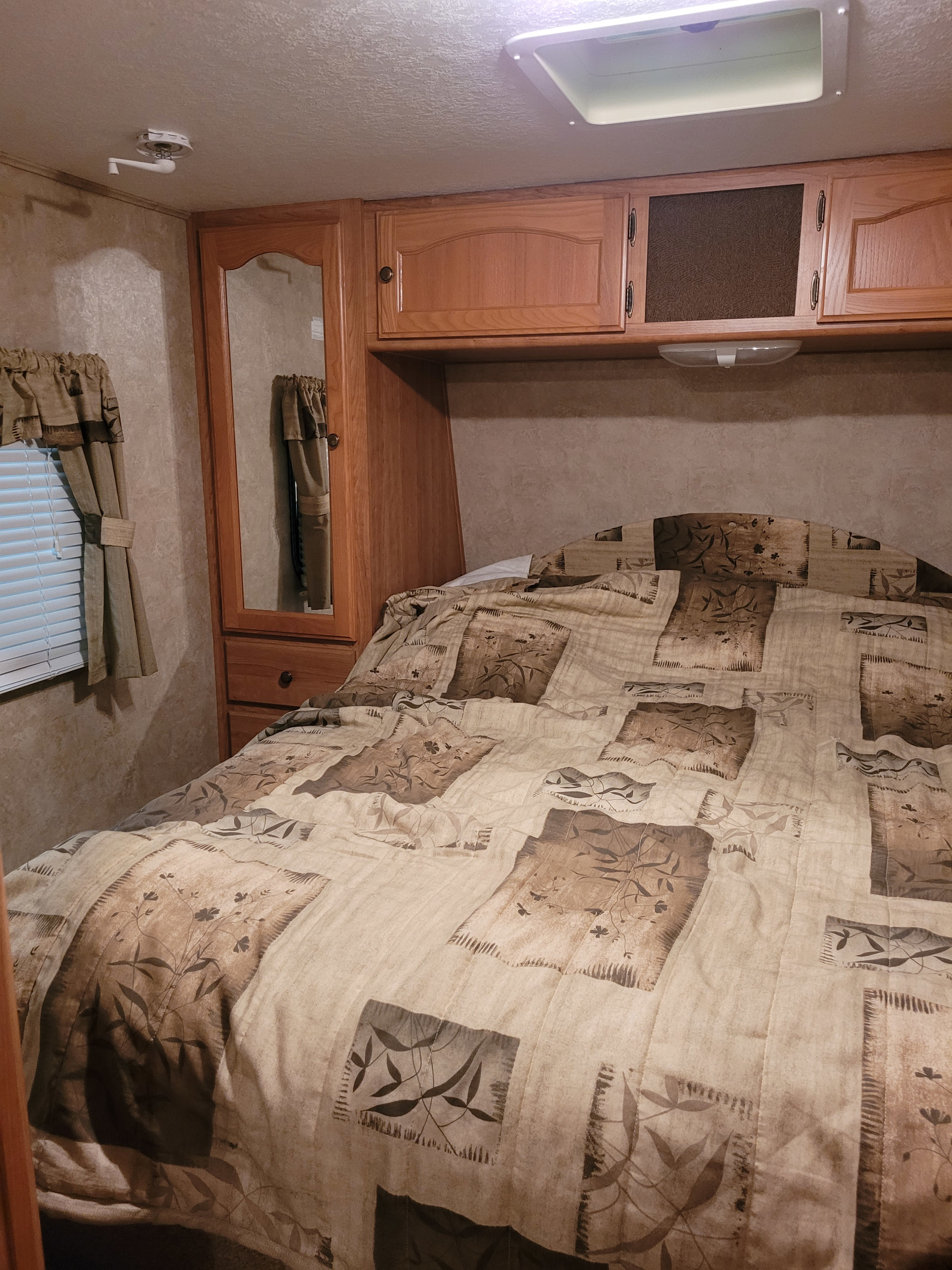 Interior of an RV rental: a cozy bedroom with patterned bedding, wooden cabinets, mirrored wardrobe, and window.. Keystone Springdale 2009