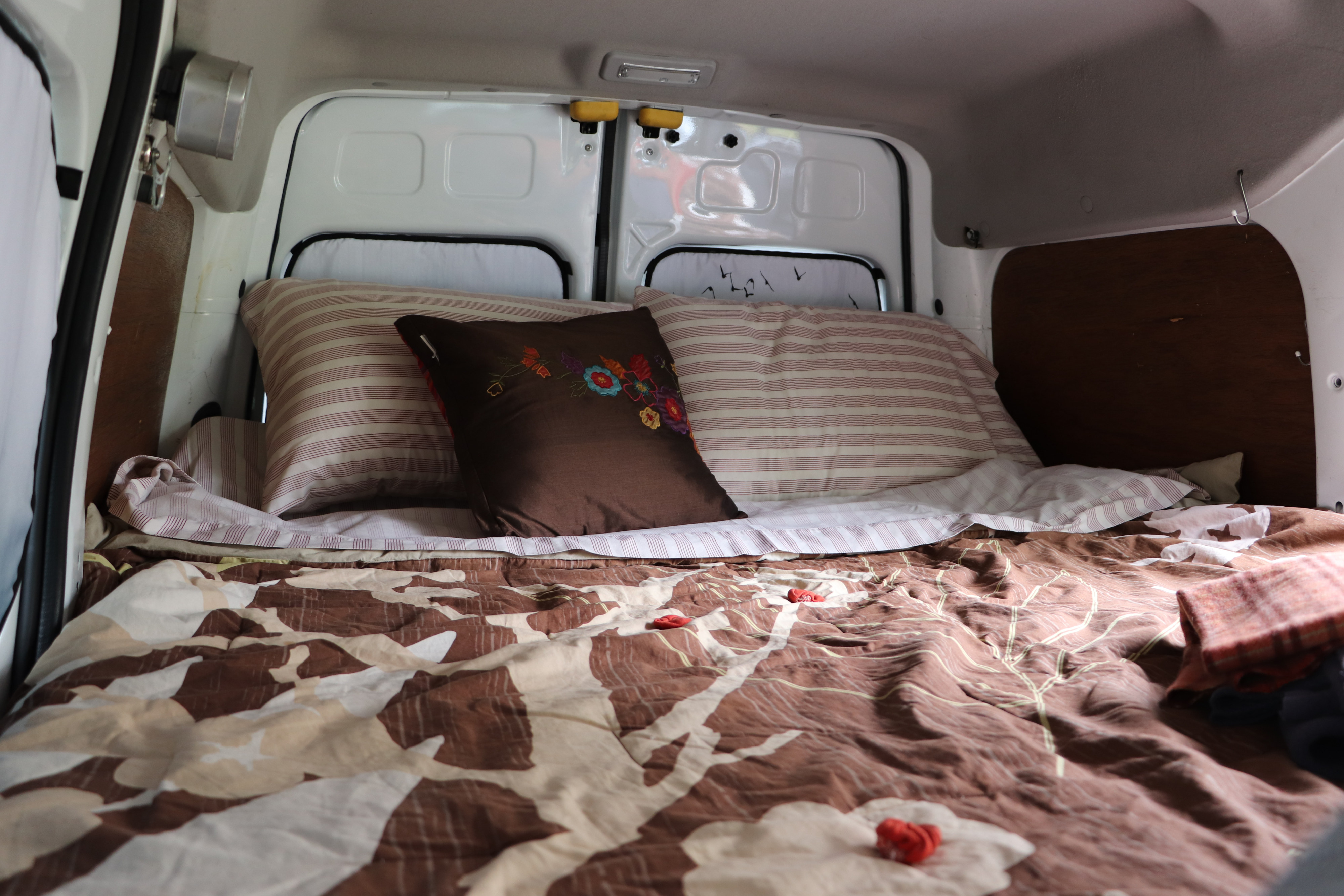 Comfortable bed inside an RV rental, featuring striped pillows and a brown patterned comforter for a cozy rest.. Ford Connect 2012
