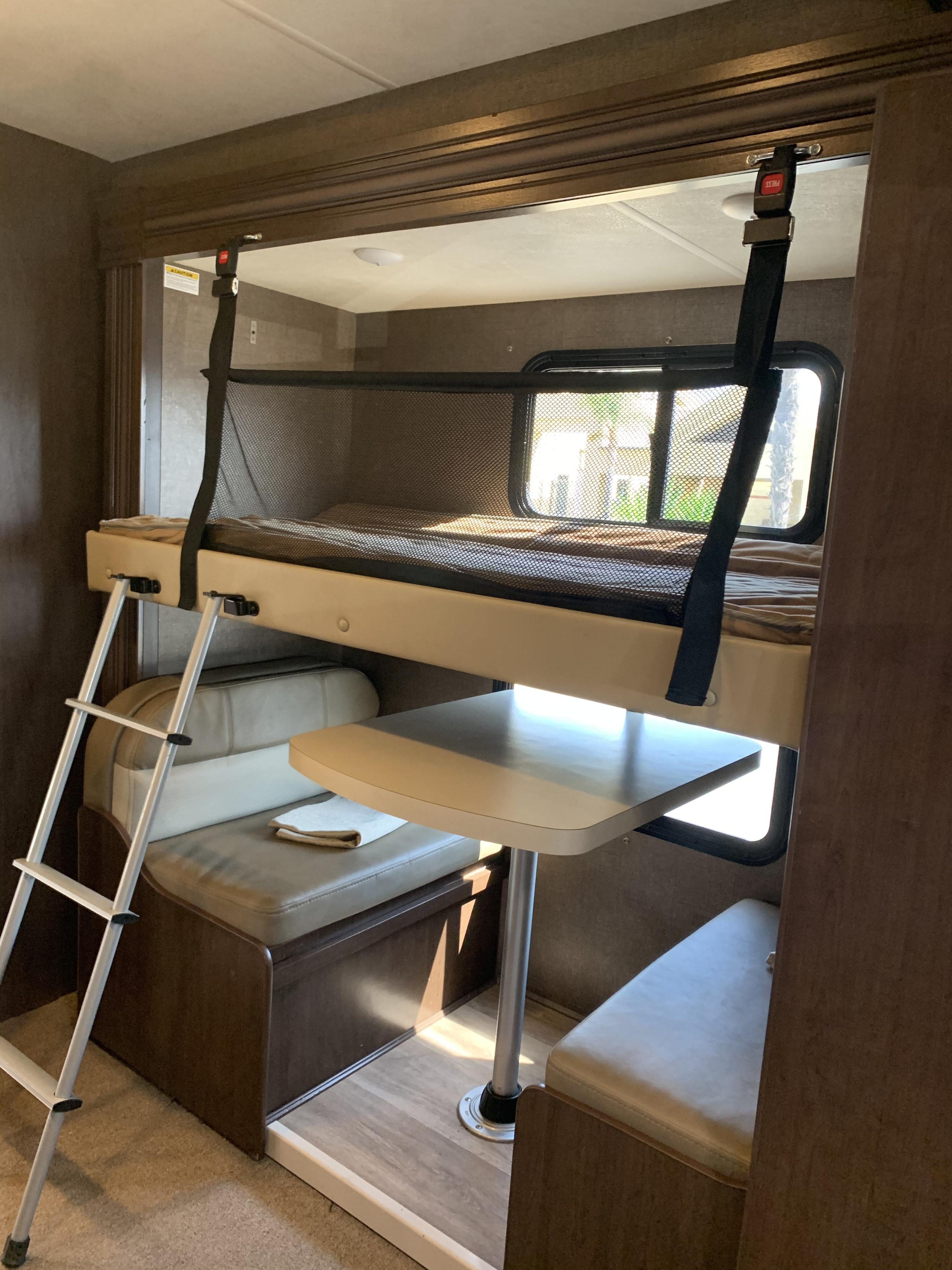 Compact RV rental interior: bunk bed with safety net & ladder over a dinette with table & bench seating.. Four winds Four Winds 2020