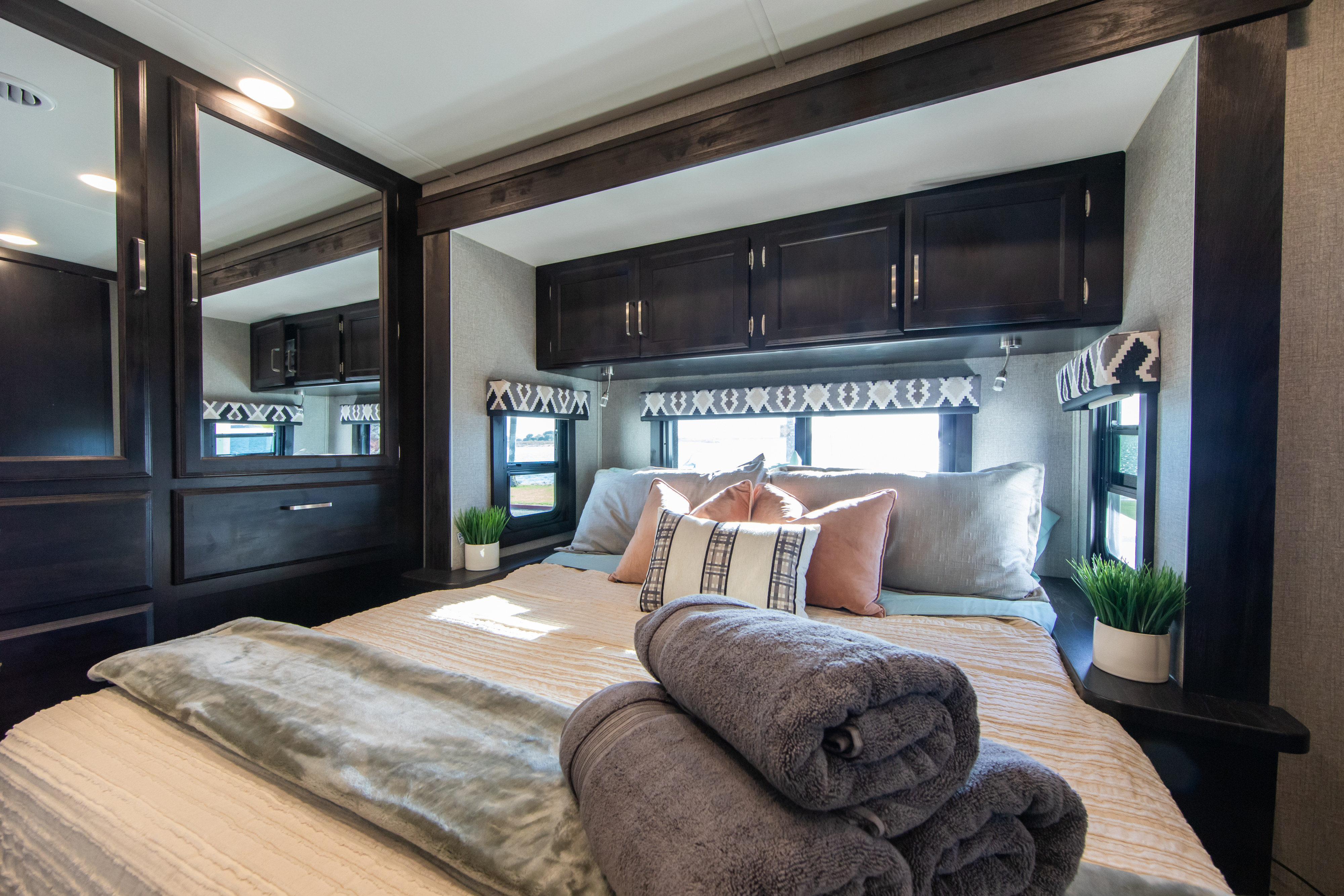 Cozy RV rental bedroom with dark wood cabinetry & mirrored wardrobe. Soft bedding, bright windows, and accent decor.. Jayco Greyhawk 2021