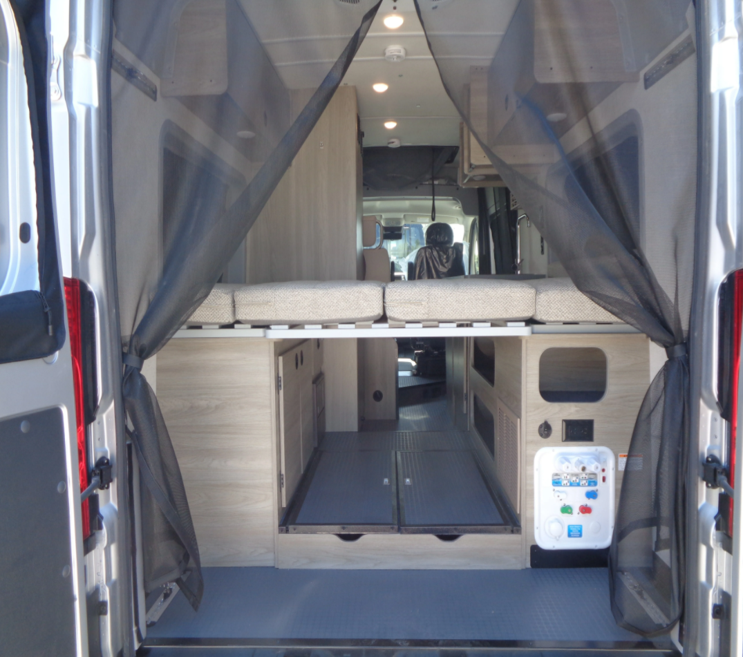 Rear view of an RV rental camper van interior, featuring an elevated bed, spacious storage area, and a control panel.. Winnebago Winnebago 2022