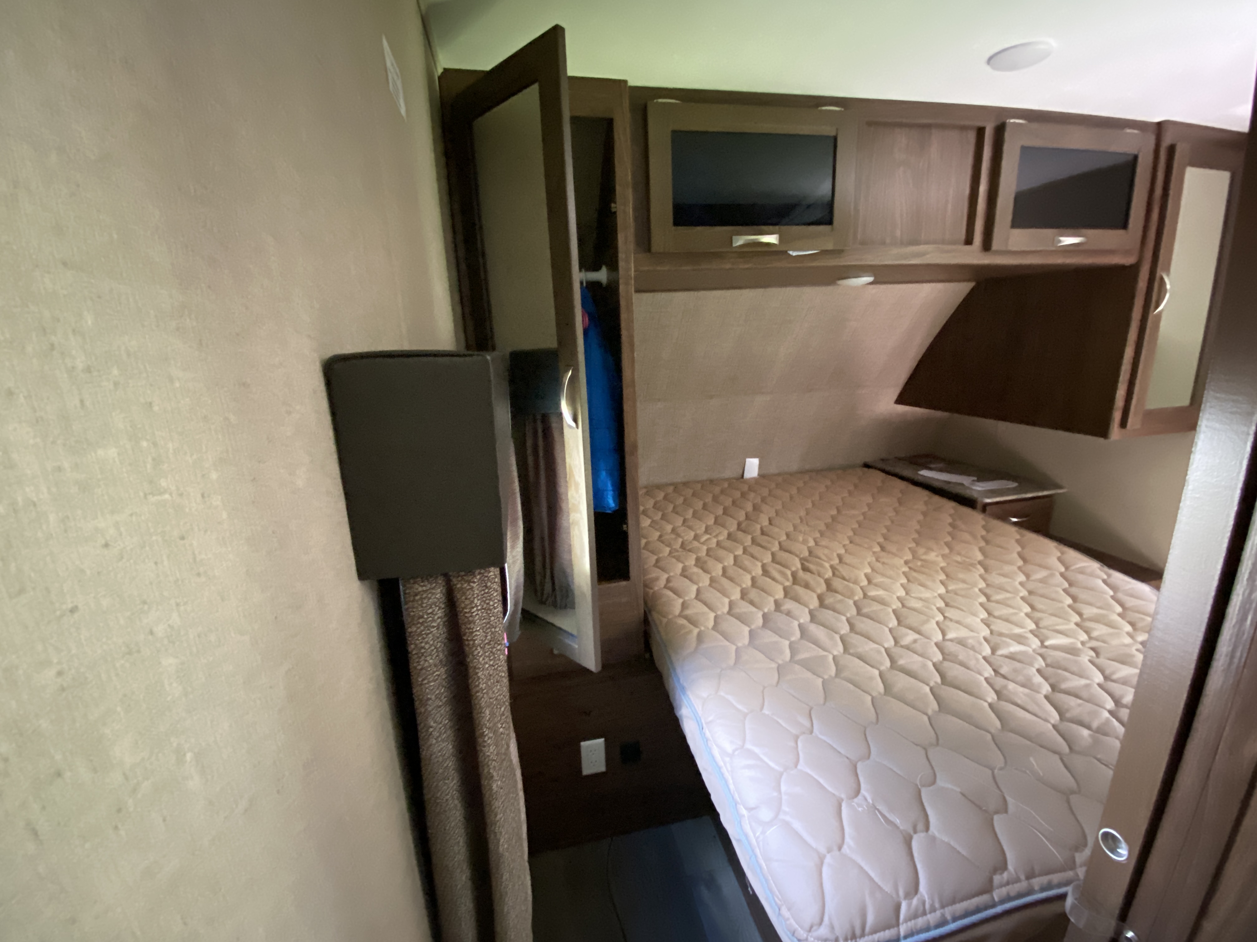 RV rental bedroom interior with a quilted bed, overhead cabinets, TV, and wardrobe.. Coleman Light 2405BH 2017