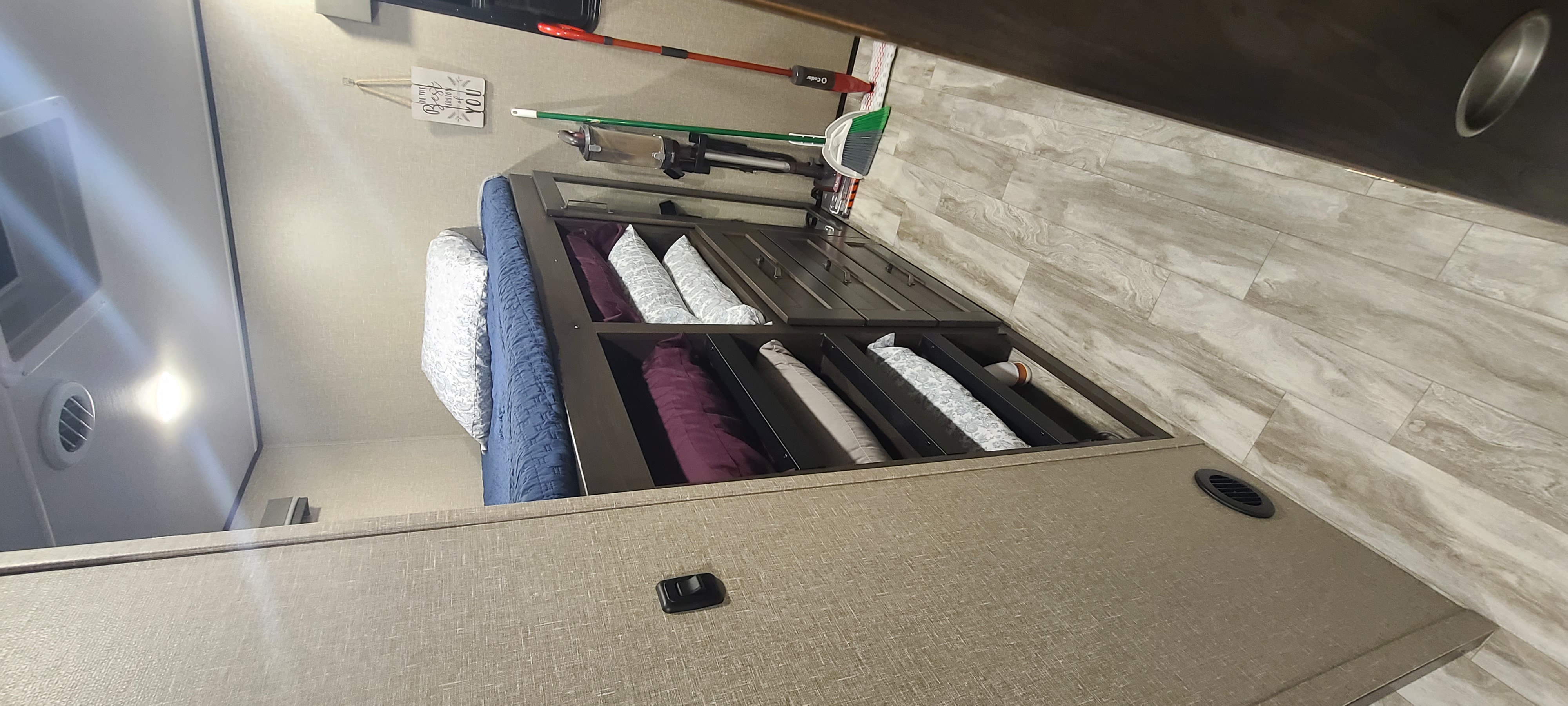 Explore this tidy RV rental bedroom: bed, built-in storage for pillows, and cleaning tools ready for your adventures.. Grand Design Reflection 2022