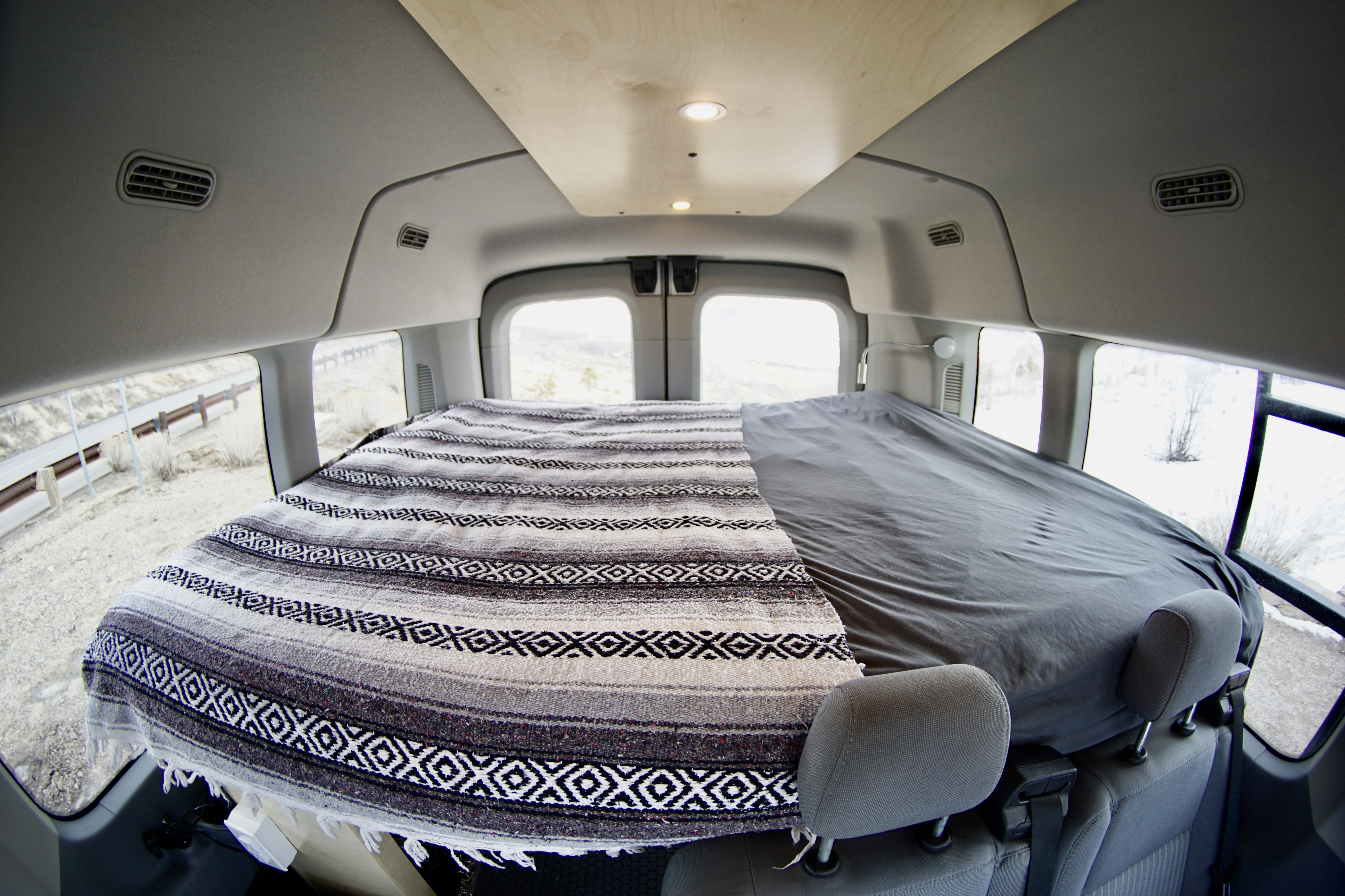 Cozy RV rental camper van interior featuring a bed with a patterned blanket, wooden ceiling, and windows showing an outdoor landscape.. Ford Transit Custom 2019