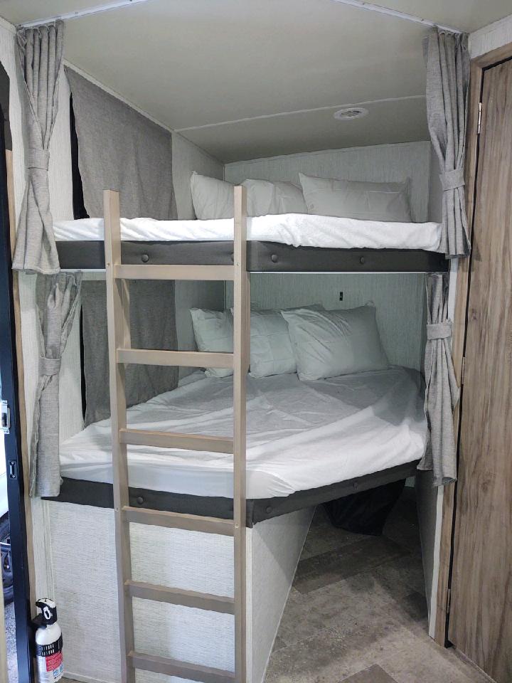 Cozy RV rental features bright, made-up bunk beds with a ladder, providing comfortable sleeping arrangements within a compact space.. Palomino Solaire 243bhs 2021